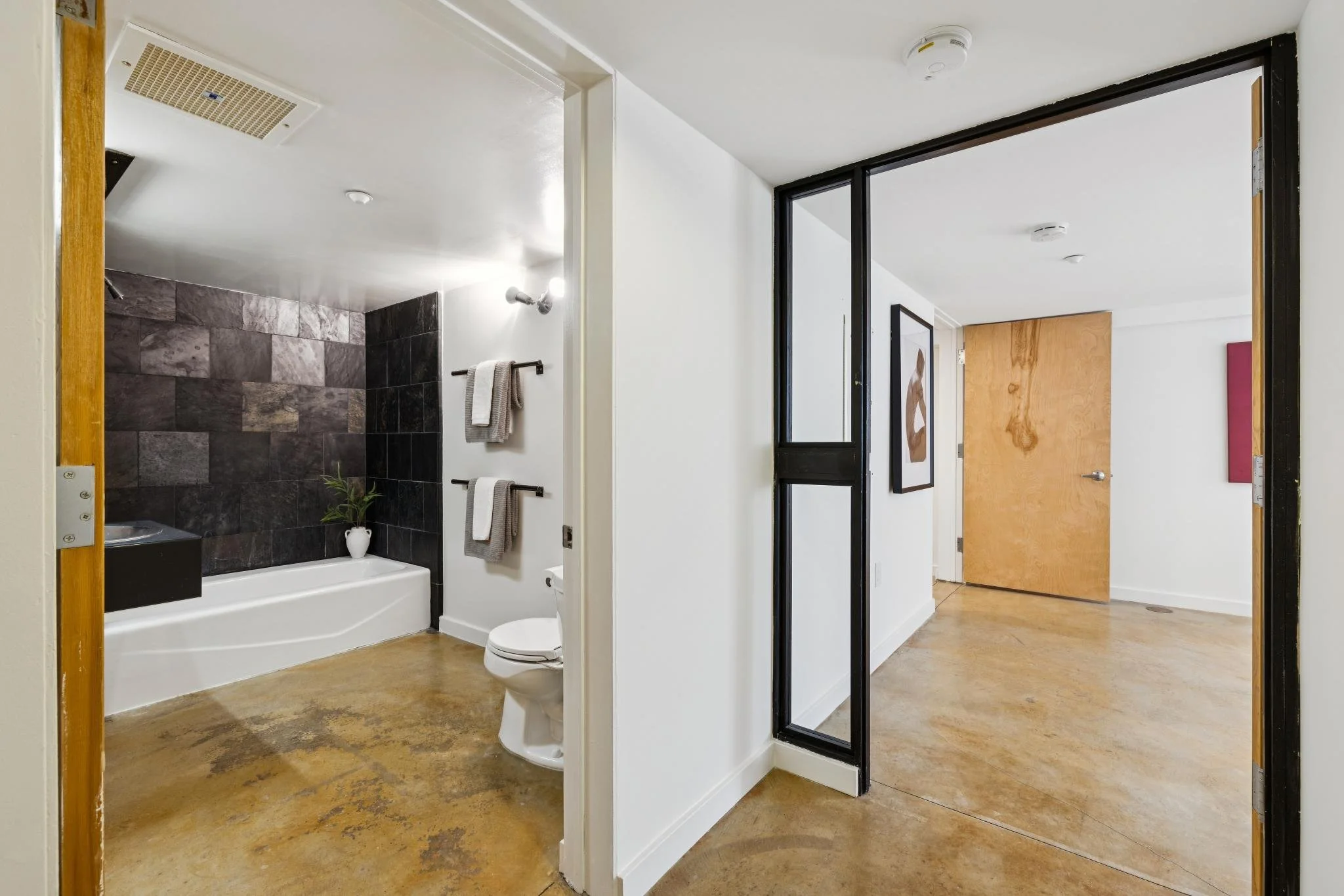 View of a bathroom with a bathtub and shower area, separated by a glass door in a modern apartment.