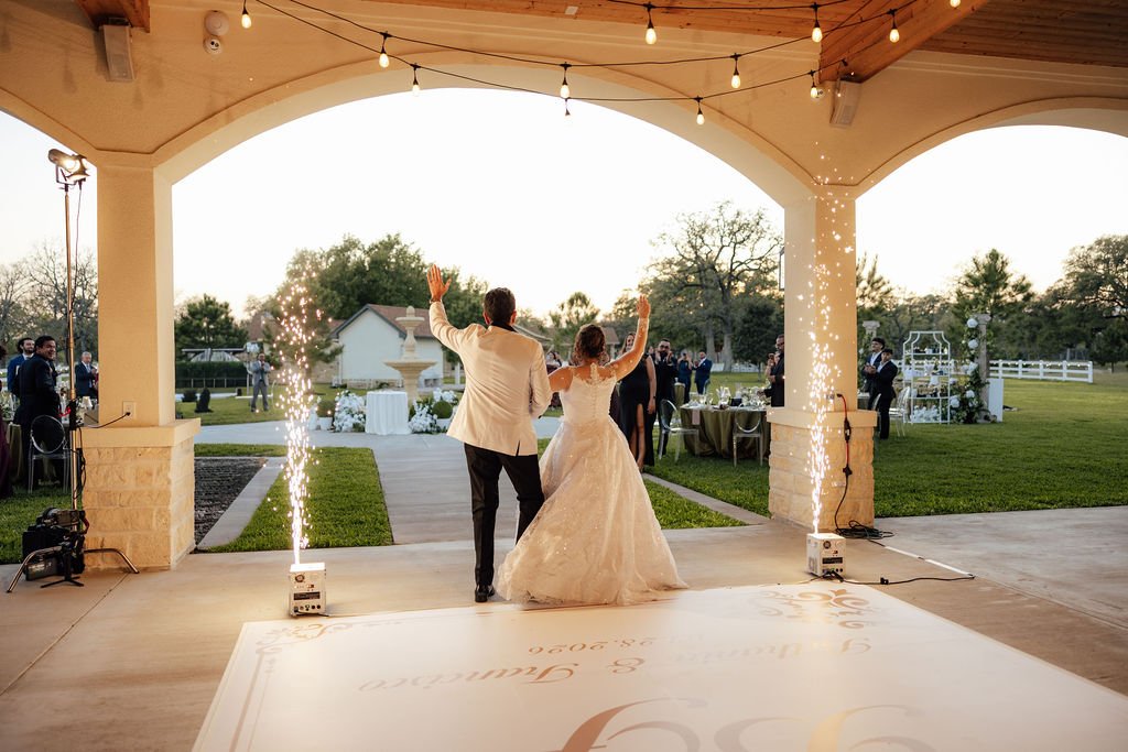 A bride and groom dancing at their wedding reception under an outdoor pavilion with string lights and sparklers overlooking their garden wedding reception.