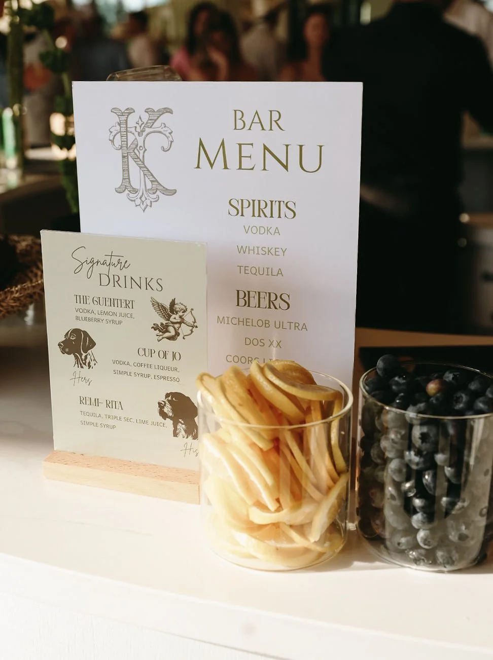 Bar menu with a list of spirits, beers, and signature drinks, placed on a table alongside bowls of lemon wedges and blueberries.