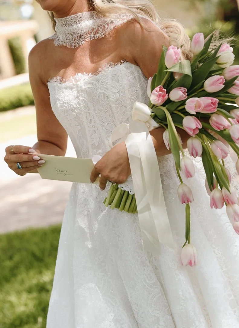 A woman in a white lace wedding dress holding a bouquet of cascading pink tulips and a heartfelt envelope.