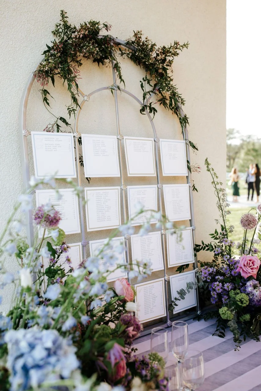 A seating chart display decorated with flowers at an outdoor wedding. 