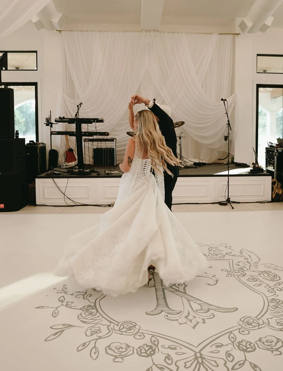 Bride and groom dancing at a wedding reception with a decorated stage and musical instruments in the background.