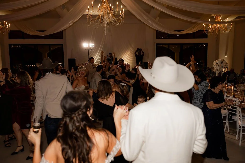 Guests dancing and celebrating at a wedding reception at Ro Manor with chandeliers, drapery, and floral centerpieces.