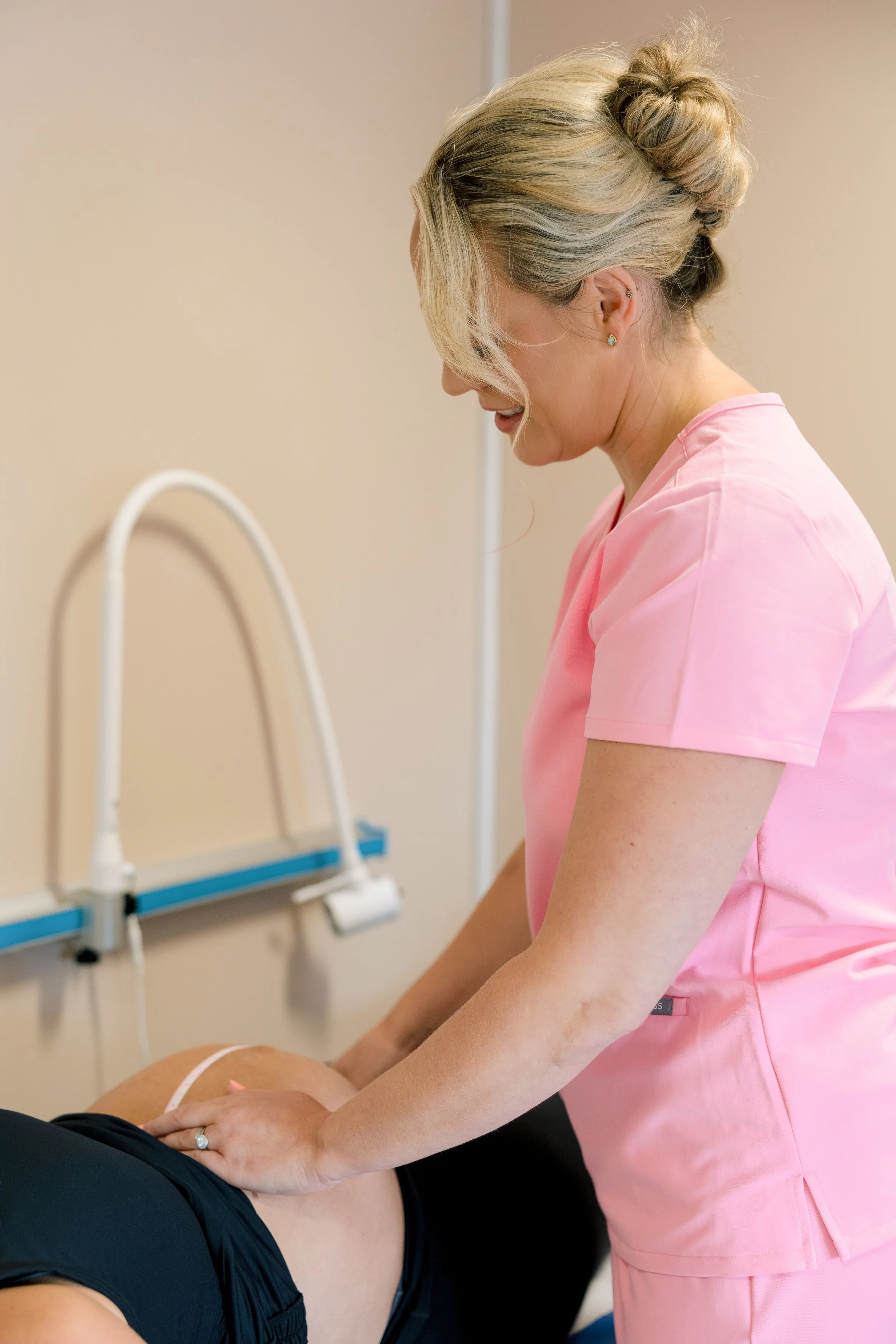 A healthcare professional in pink scrubs giving a chiropractic adjustment to a patient lying face down on a treatment table.