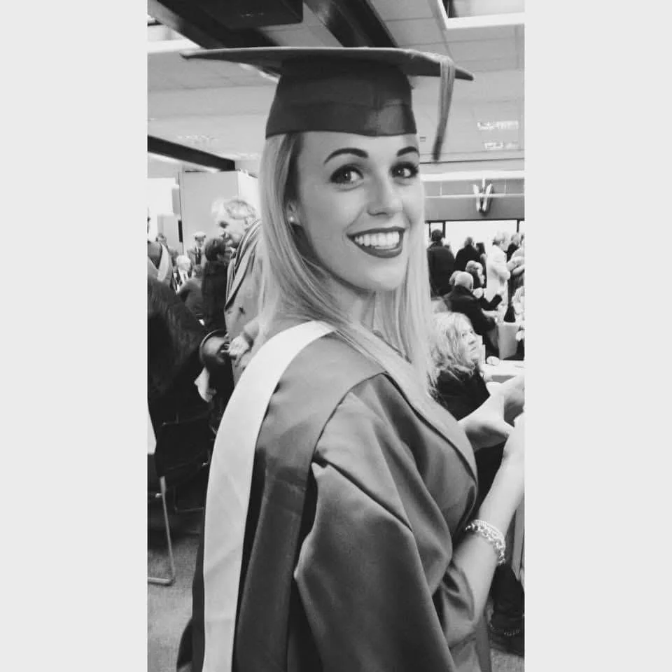 A young woman in graduation cap and gown smiling at a graduation ceremony.
