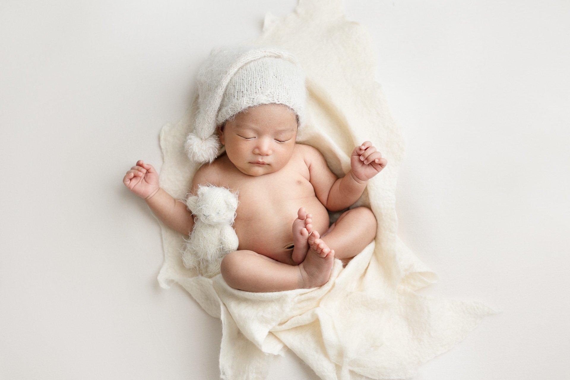 Light and airy newborn boy photographed in Victoria BC, sleeping on a cream blanket with small teddy bear SophiePhoto