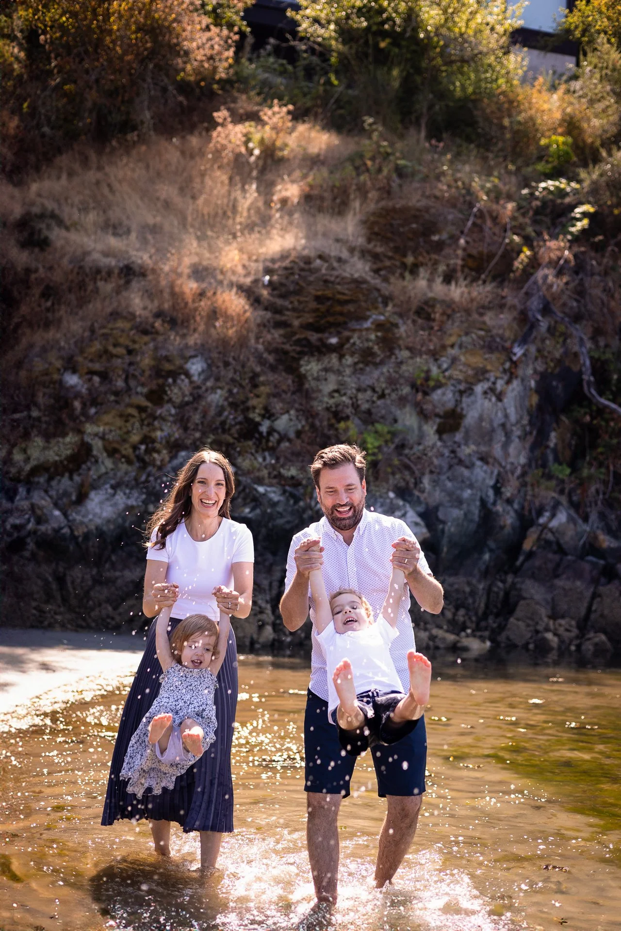 Summer beach family session in Victoria with mom and dad swinging their two boys on the shoreline. Photographed by Sophie Lecavalier of SophiePhoto