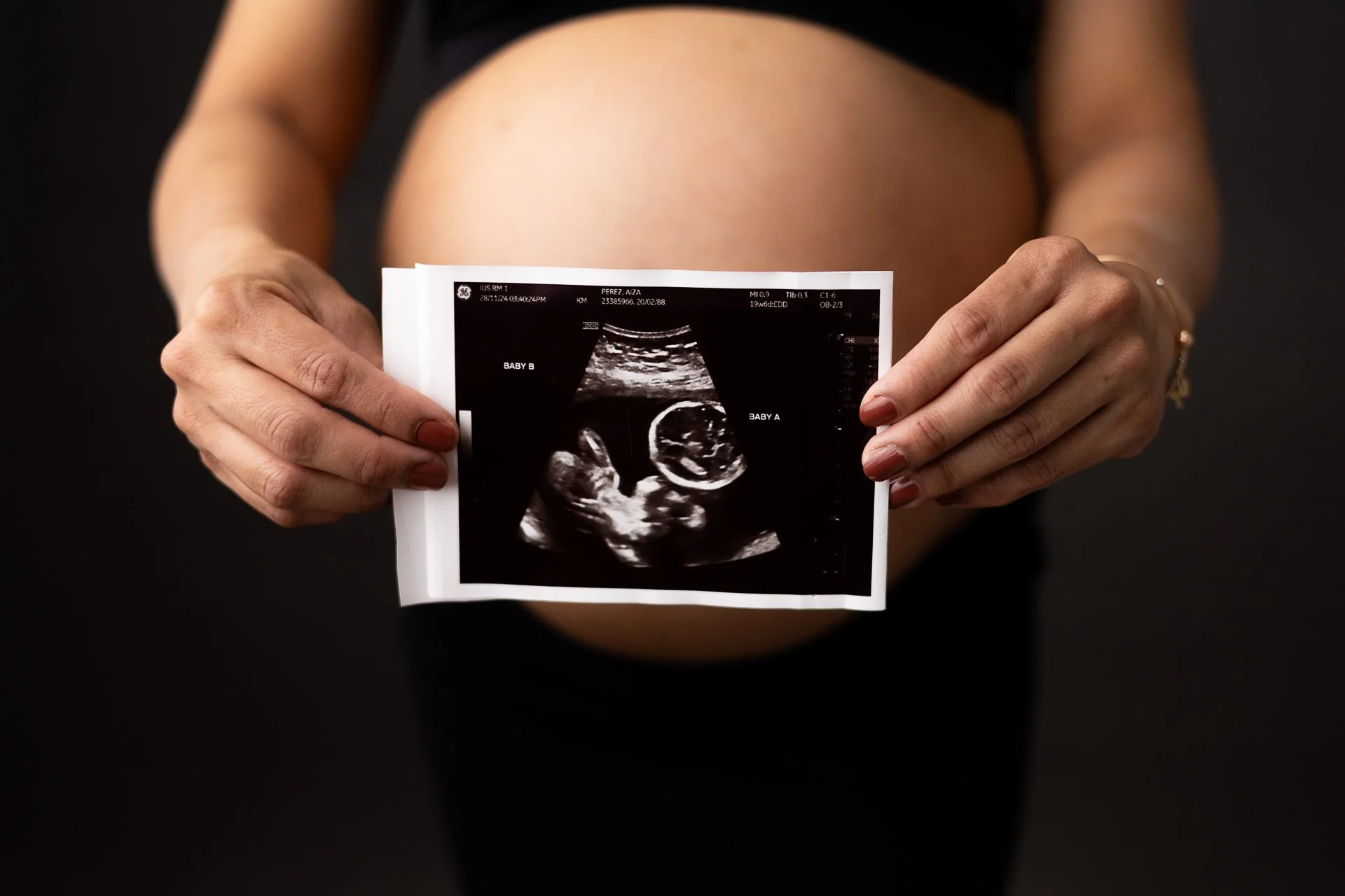 Studio maternity session with Sophie Lecavalier Photography: mom is on a dark backdrop, holding a photo of the baby's sonogram in front of her bare belly