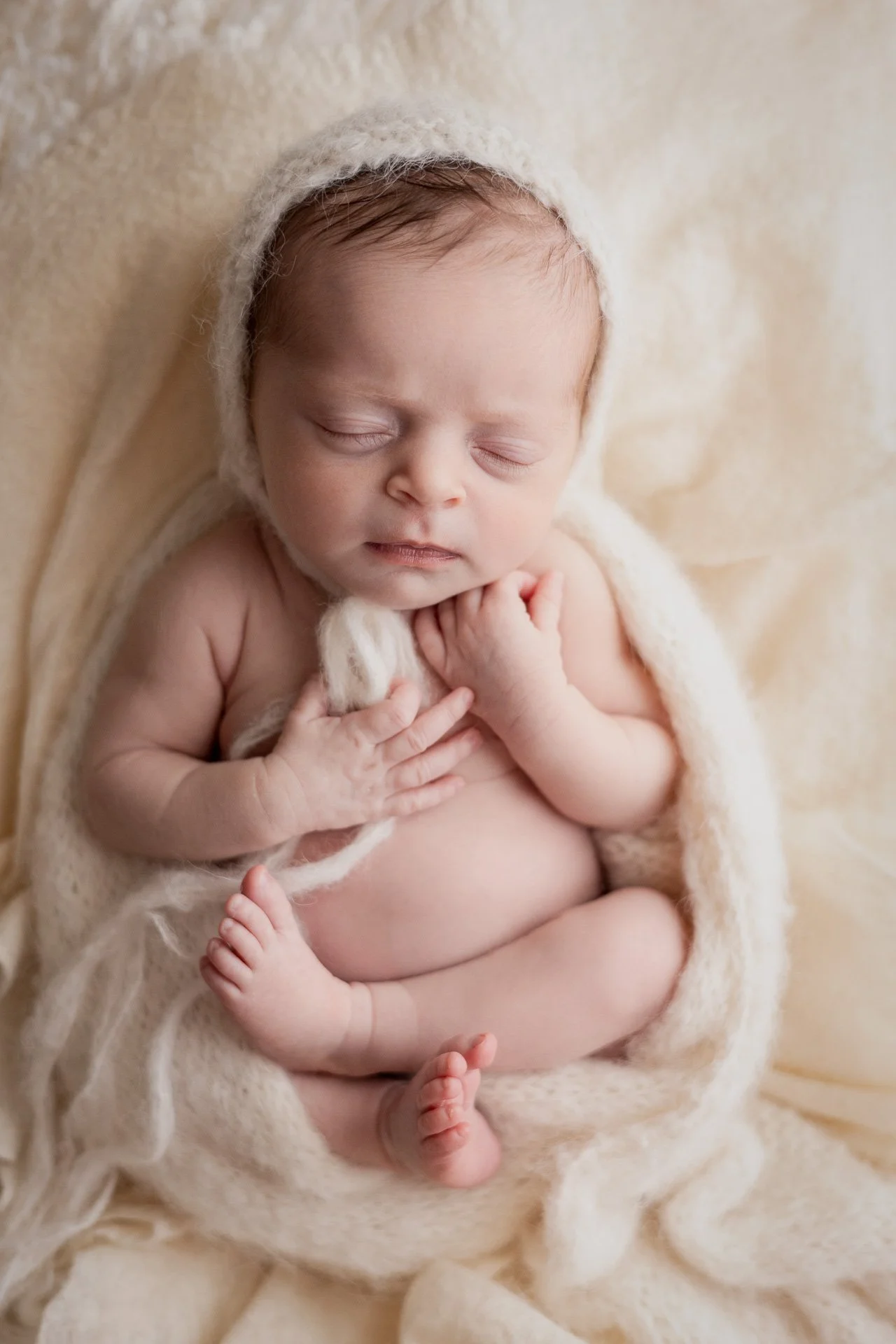 Fair-haired baby wrapped in soft Ivory blanket with matching bonnet all curled up Sophie Lecavalier photography