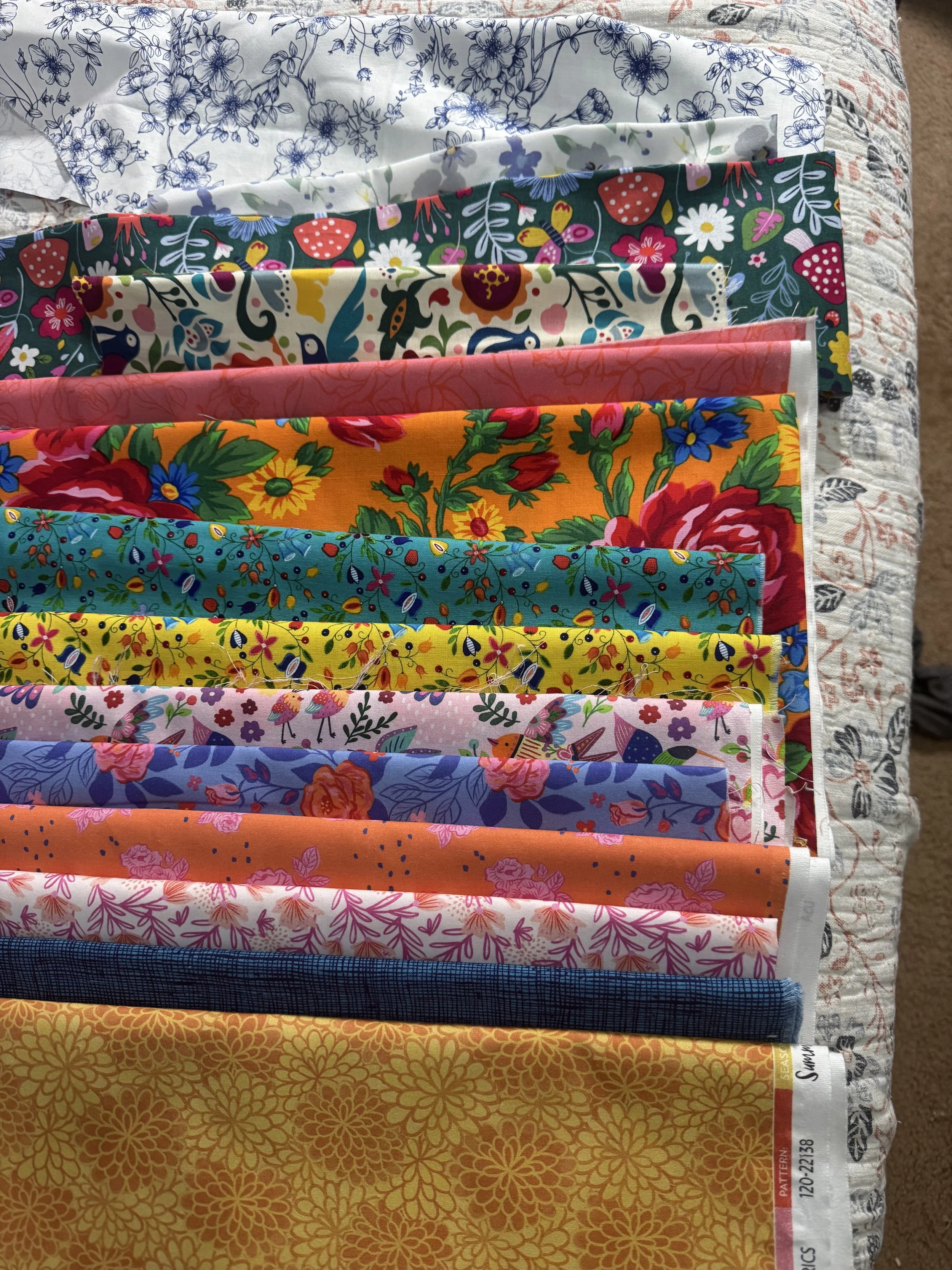 A collection of colorful fabric pieces with various floral and nature-inspired patterns laid out on a surface.