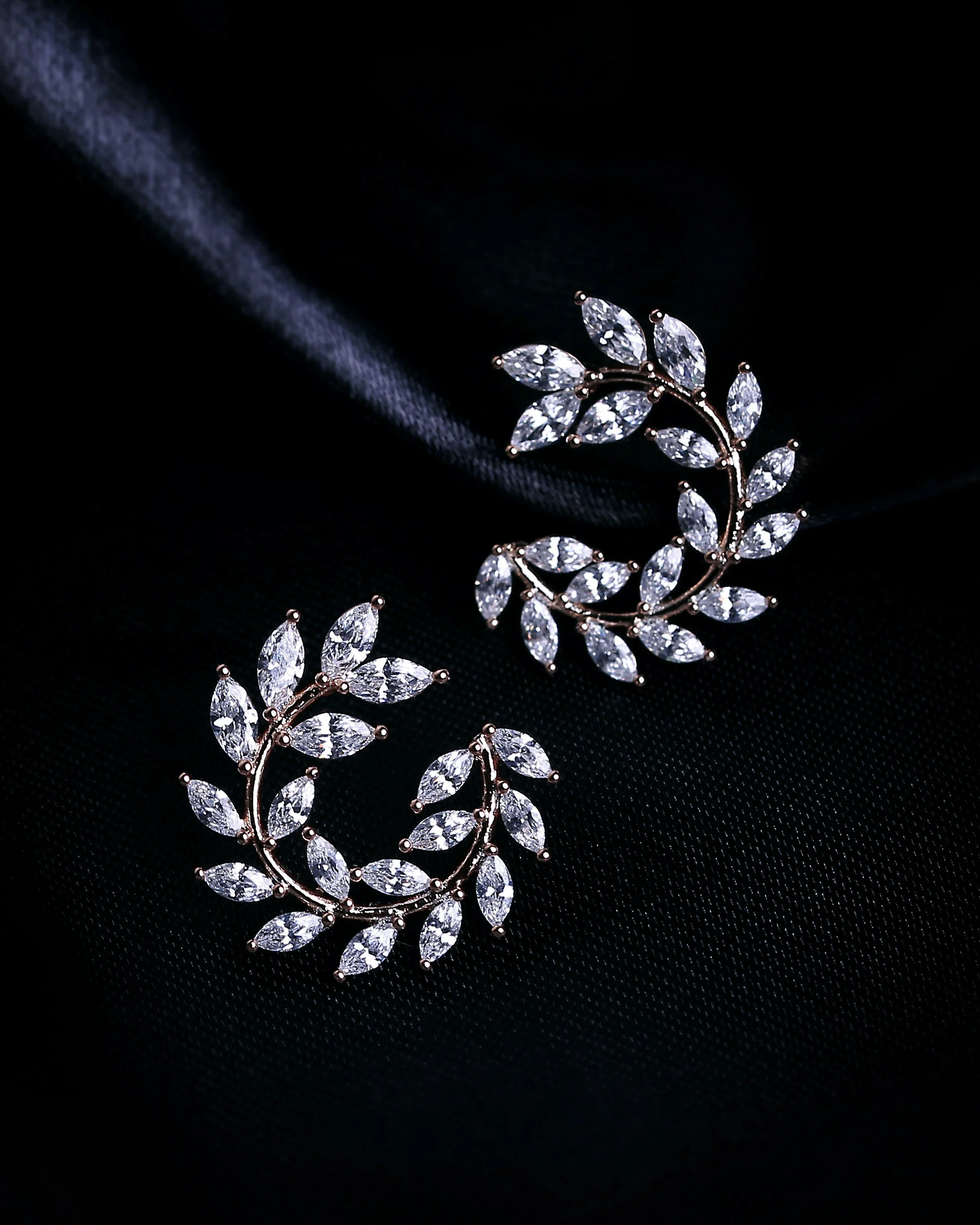 A silver jewelry piece with leaf-shaped clear gemstones arranged in a circular pattern on a black background.
