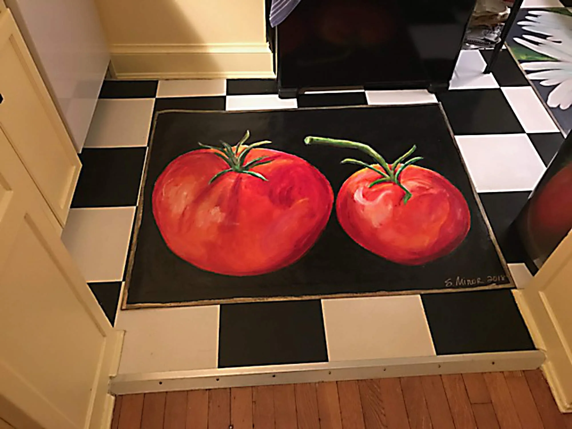 A black table with a painting of two large red tomatoes with green stems, placed on a kitchen countertop with black and white checkered tiles.