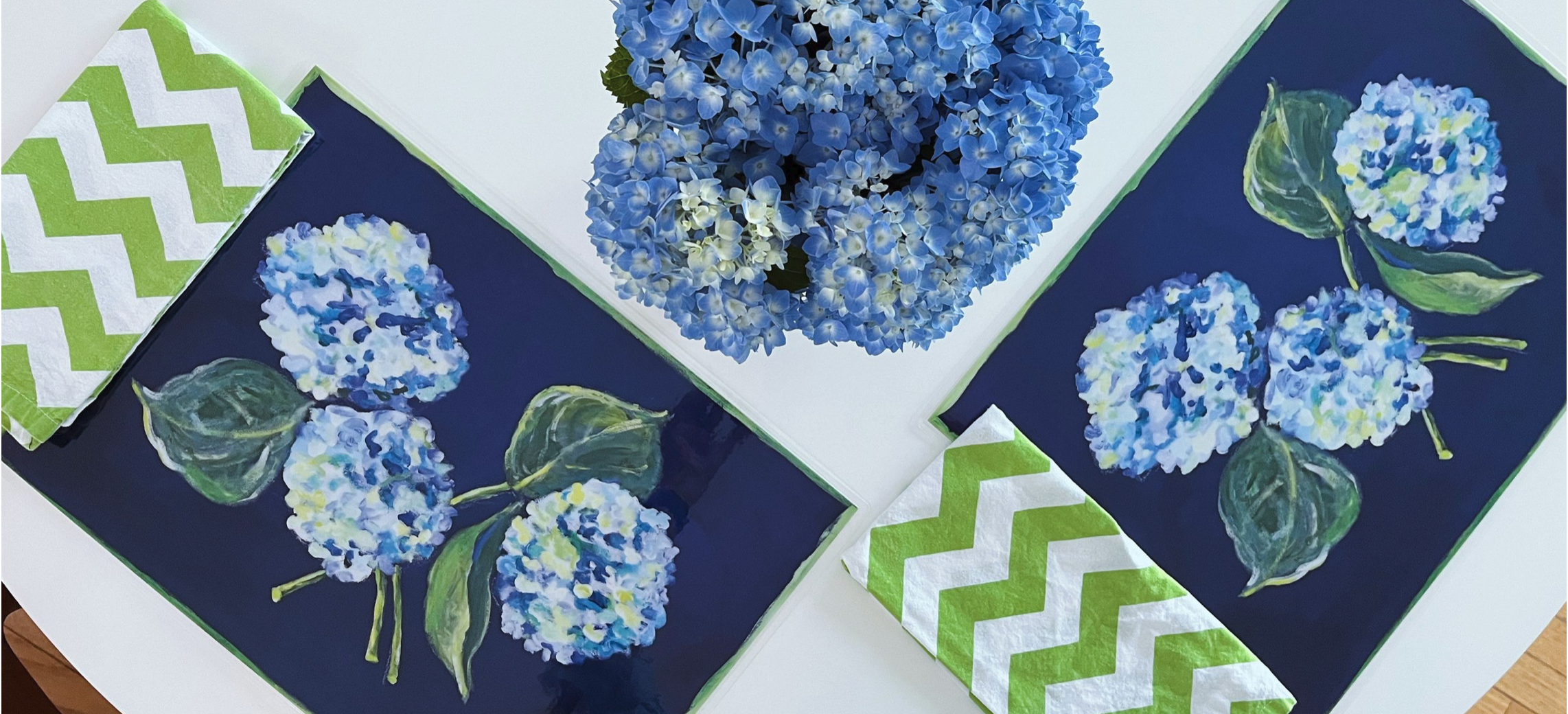 Blue hydrangea flowers on navy and white botanical plates with matching napkins, arranged on a white surface.