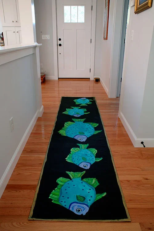 Hallway with wooden floor and hand-painted canvas runner of colorful blue fish on black background
