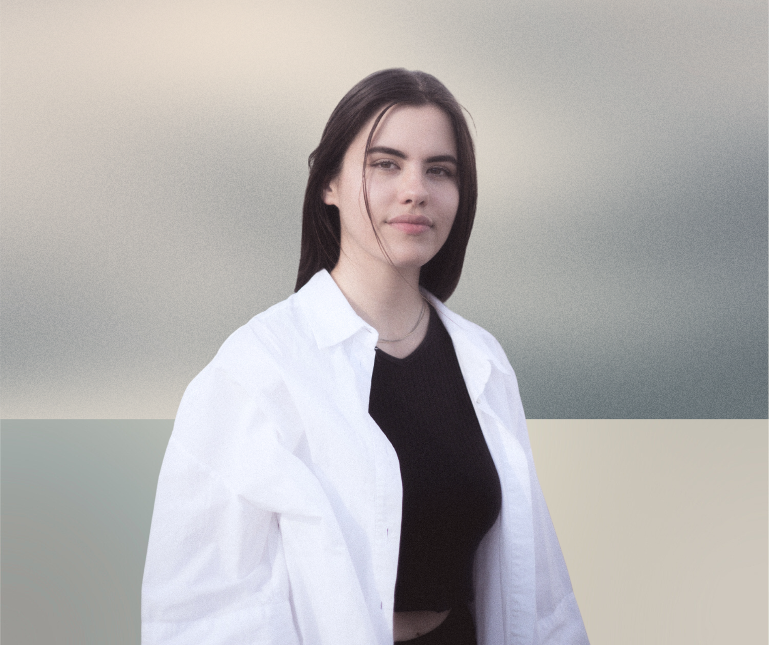 Eine junge Frau mit dunklen Haaren trägt ein schwarzes Oberteil und eine weiße offene Hemdjacke, steht vor einem pastelfarbenen, abstrakten Hintergrund.