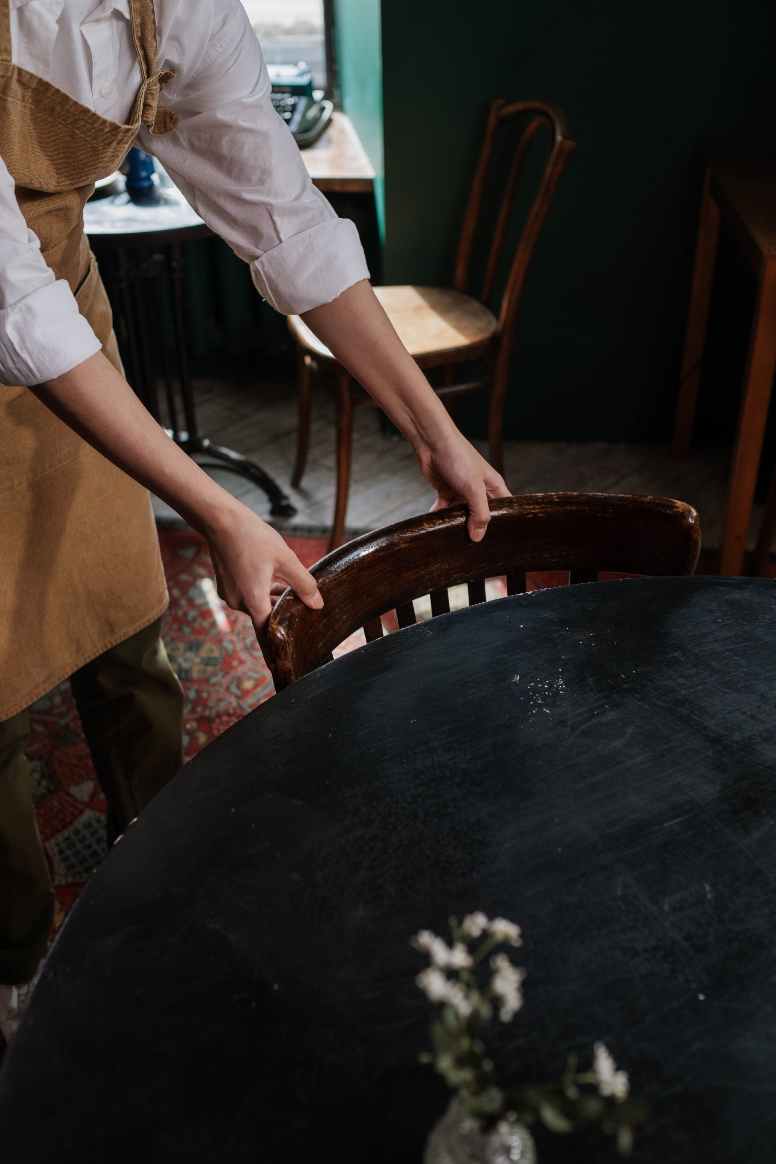 Persona colocando sarten en mesa de cafetería. Fondo con sillas y mesa, ambiente acogedor en establecimiento de comida.