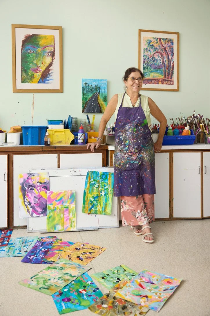 Dena Lawrence in her art studio, surrounded by paintings and materials.