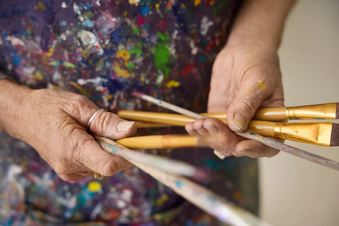 Hands holding a collection of paintbrushes in the studio.