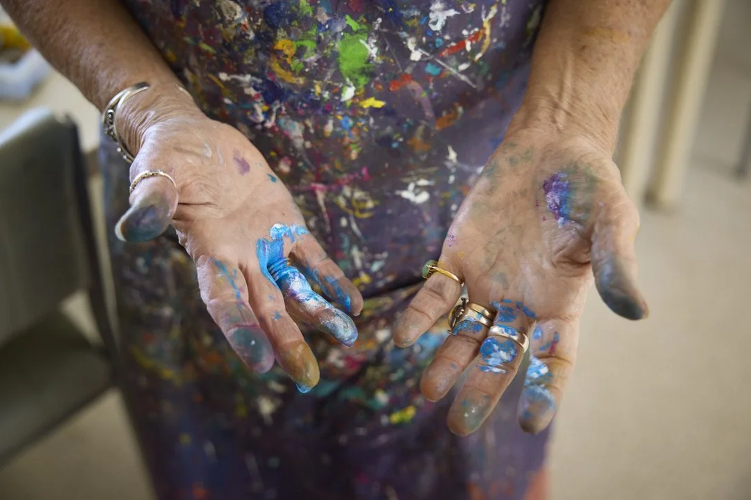 Open hands marked with blue and purple paint in front of a paint-splattered apron.