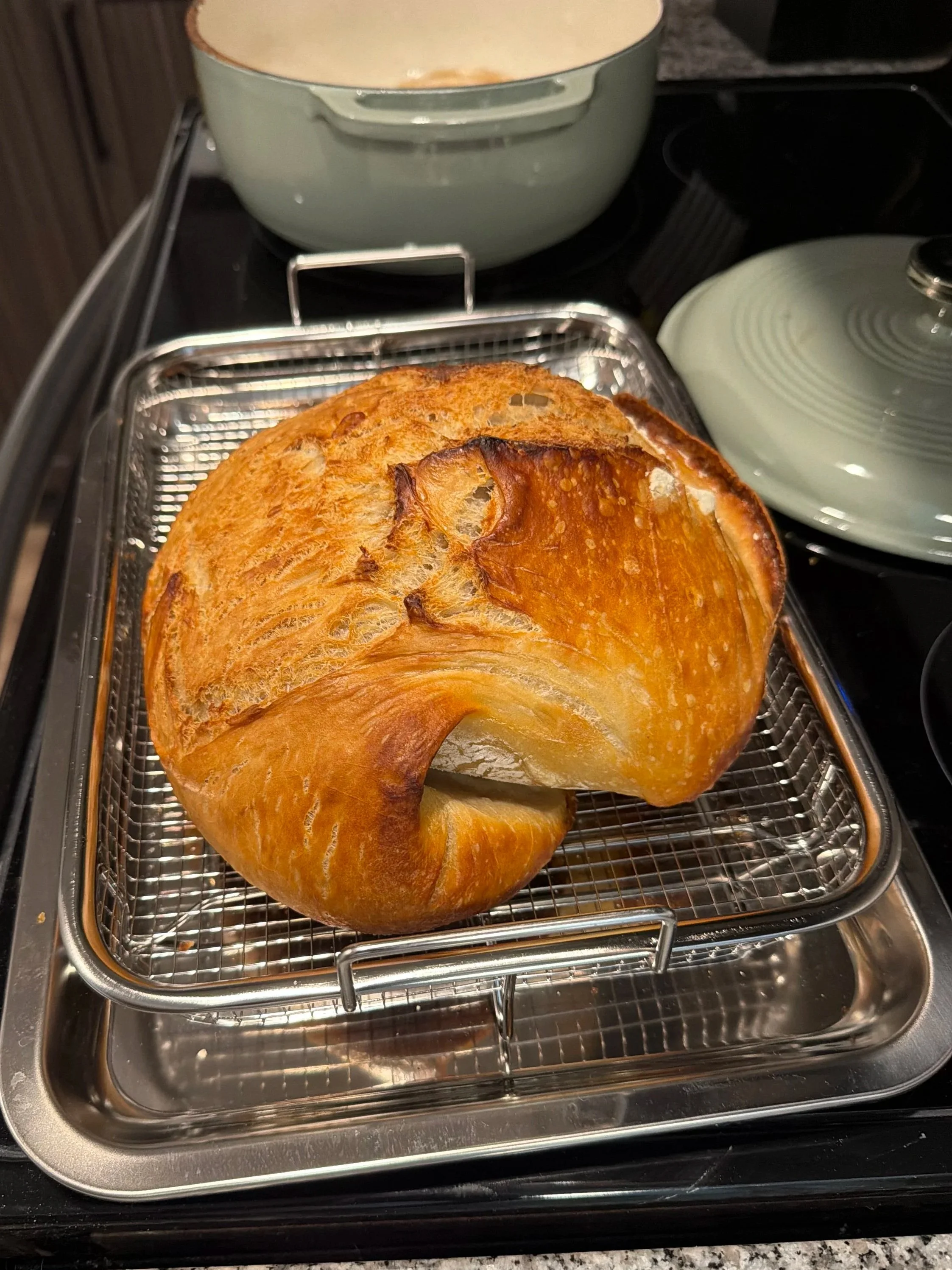 A loaf of bread cooling on a wire rack inside a toaster oven.