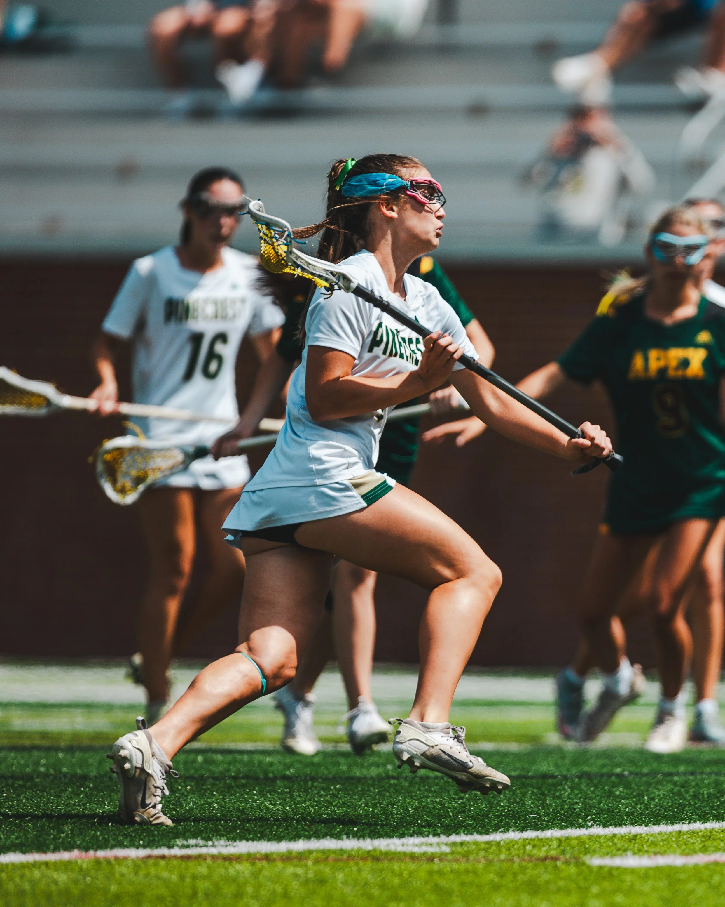 Female lacrosse players in athletic gear running on a field during a game.