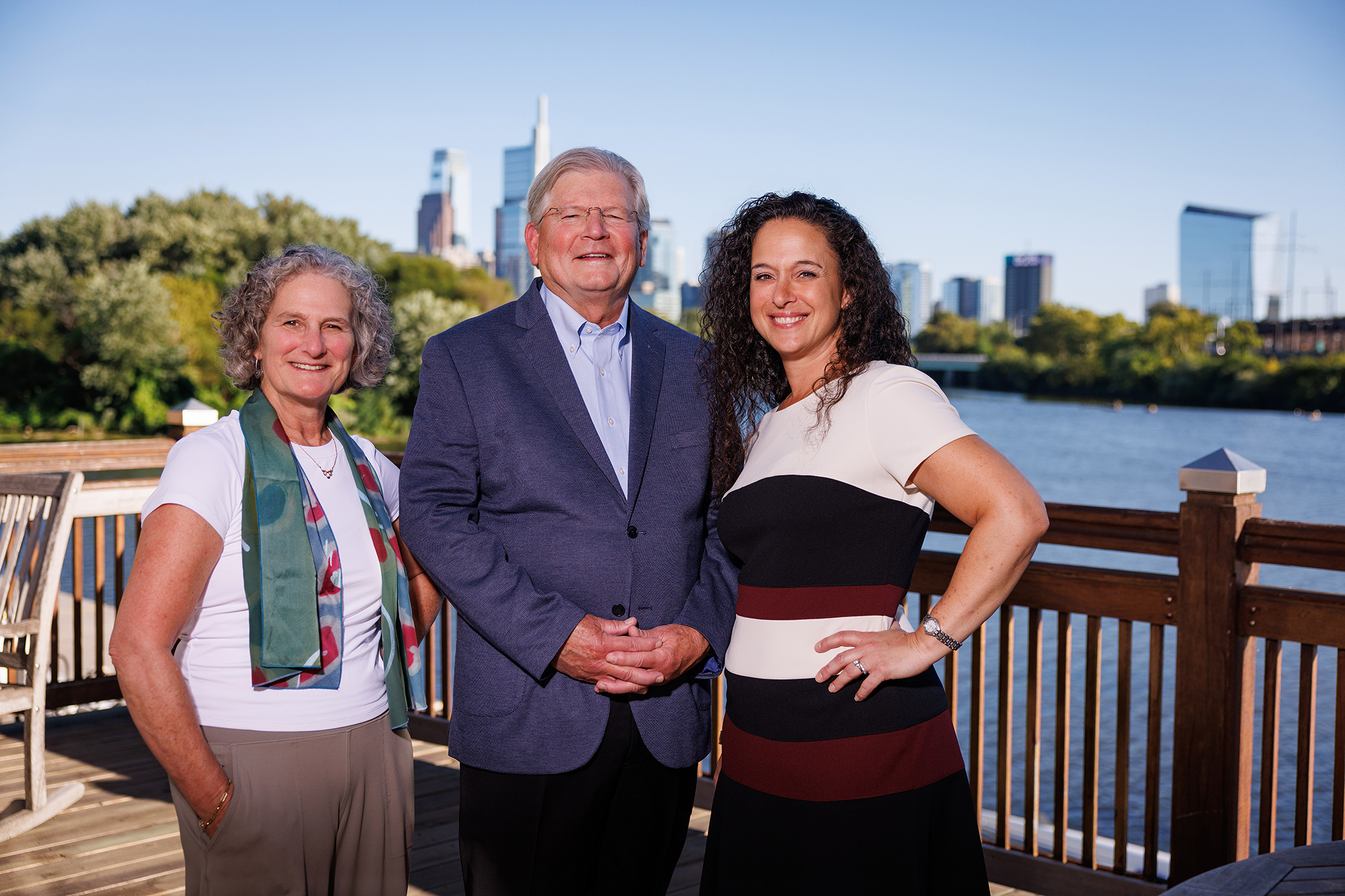 Amy, Jim, and Mariana standing on a wooden deck with the Philadelphia skyline in the background.