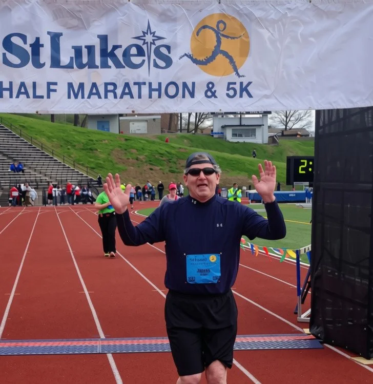 Jim Rohn crossing finish line at St. Luke's Half Marathon & 5K, with arms raised in celebration.
