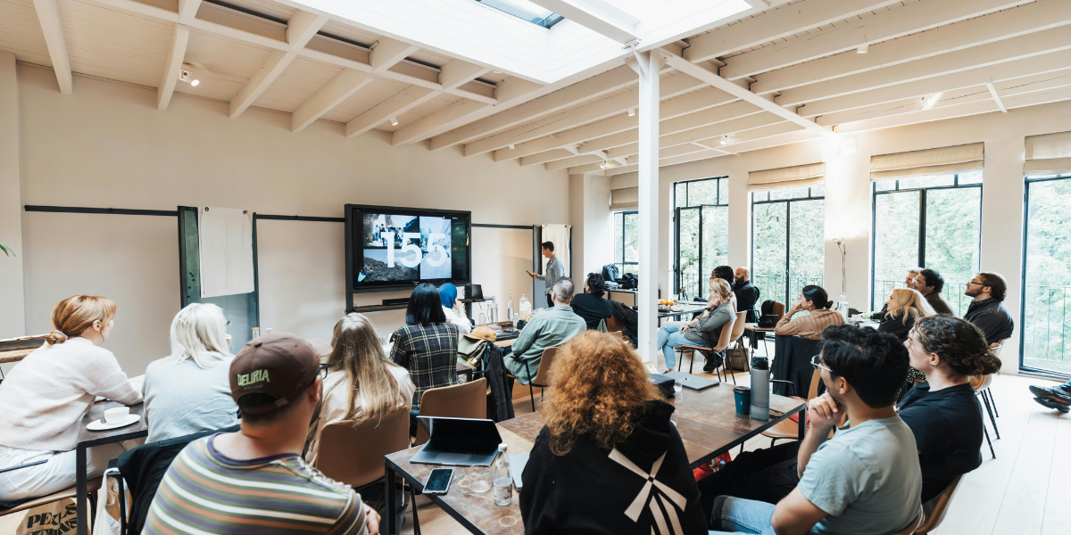 People attending a NowHuman Leadership Coaching presentation in a bright, modern conference room with large windows and a ceiling skylight.