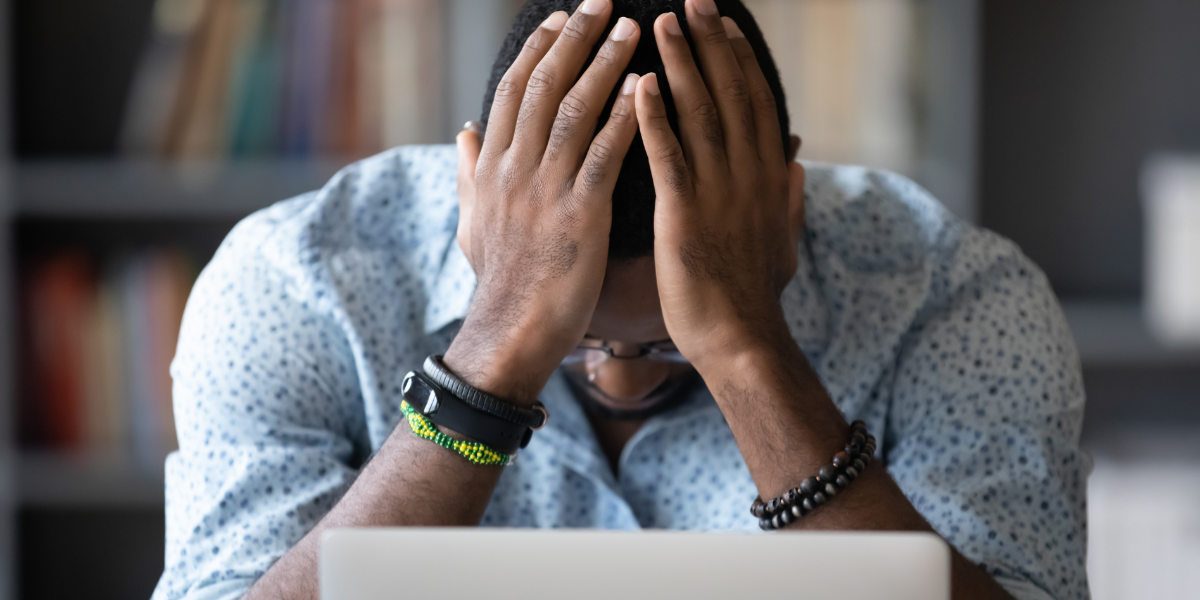 A business owner sitting at a desk with his head in his hands, looking down, possibly feeling stressed or overwhelmed about all the growing pains the business and the leadership is going through.