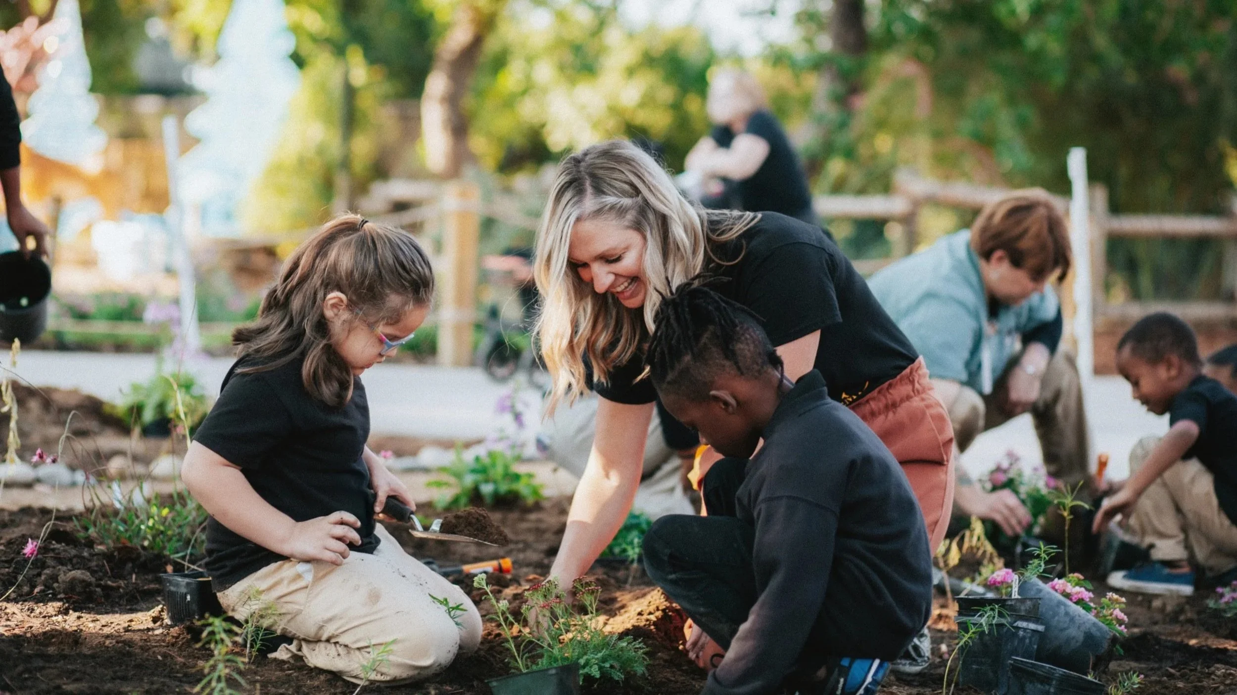 Group of children and a woman planting flowers in a garden.