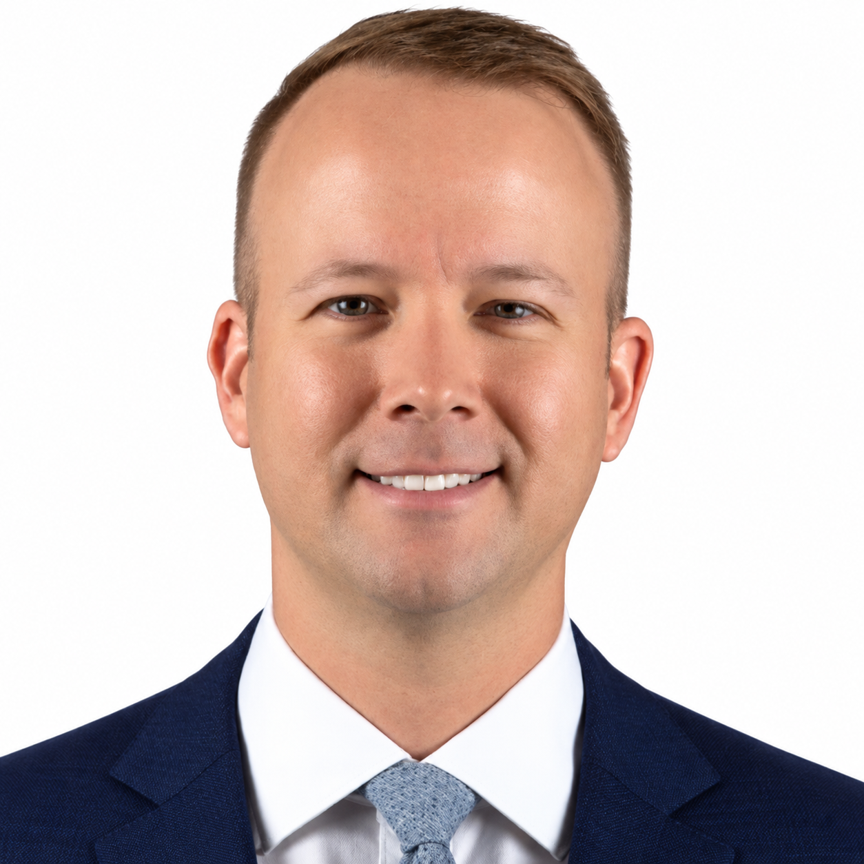 Headshot of a smiling man in a dark suit, white shirt, and light tie against a white background.