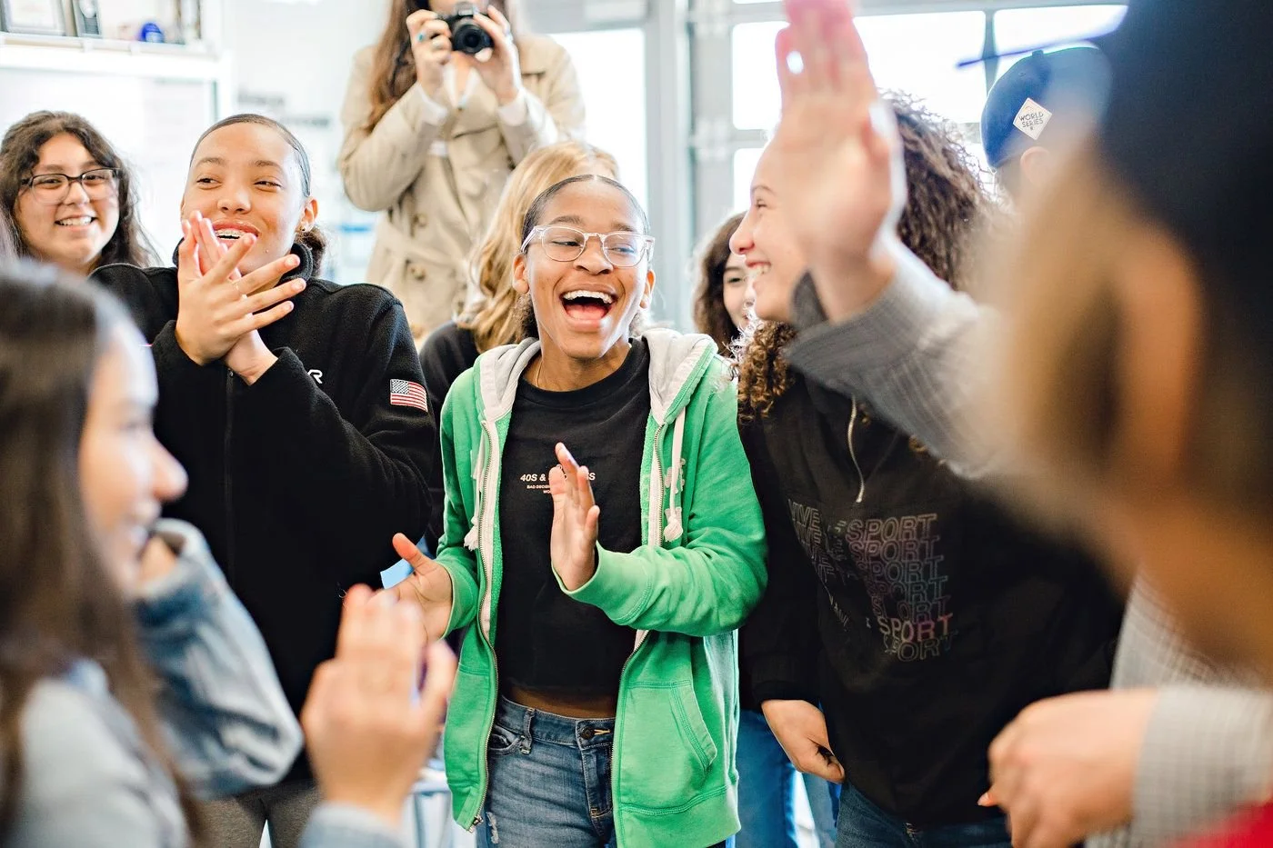 Group of children and teens laughing and having fun together, some clapping and high-fiving in a bright indoor space.