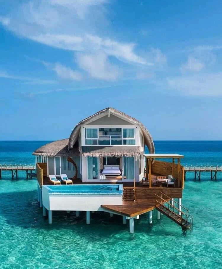 Overwater bungalow with pool, wooden deck, lounge chairs, and ocean view at tropical resort.
