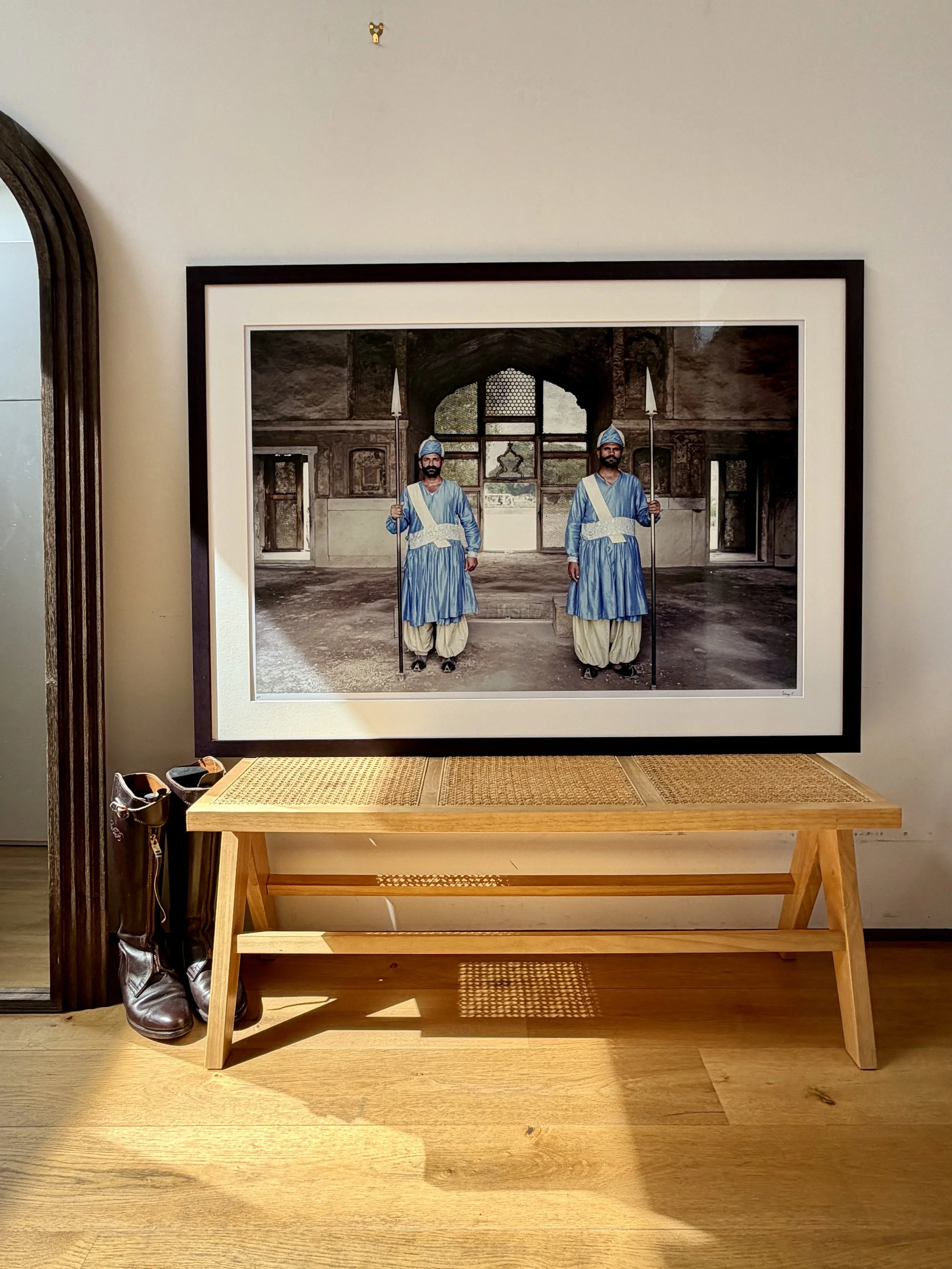 A framed photograph depicting two guards in traditional blue and white uniforms in Lahore, Pakistan, standing inside athehistoric fort with ornate architecture and large windows.