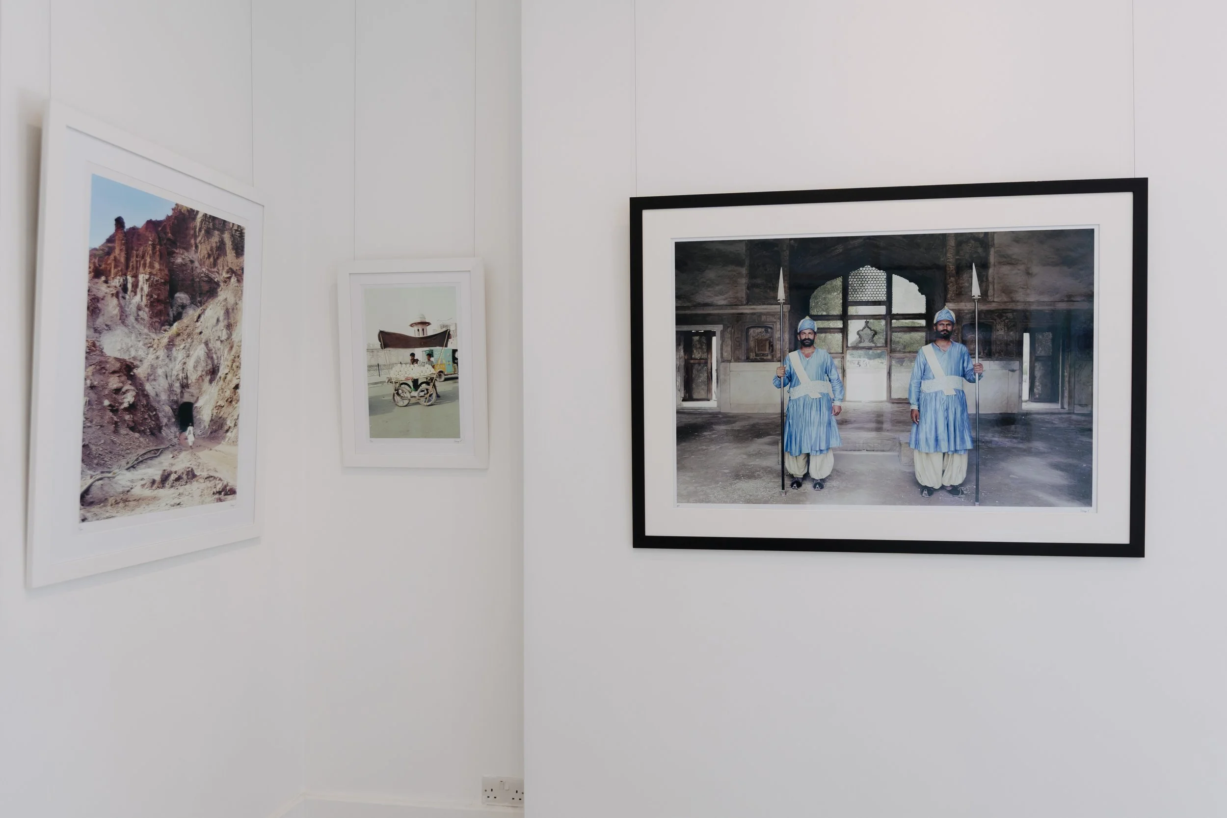 Photograph display of three framed photographs on a white gallery wall, with the rightmost image showing two men dressed in traditional Indian attire, standing inside a historical building. bELONGING, sabaya verger first exhibition