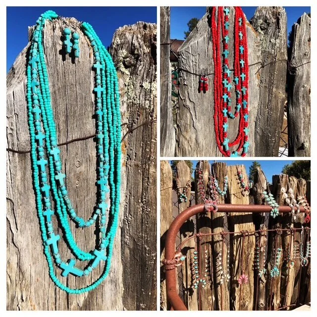 Three sets of beaded necklaces hanging on a weathered wooden fence, featuring turquoise, red, white, and pink beads in various styles.