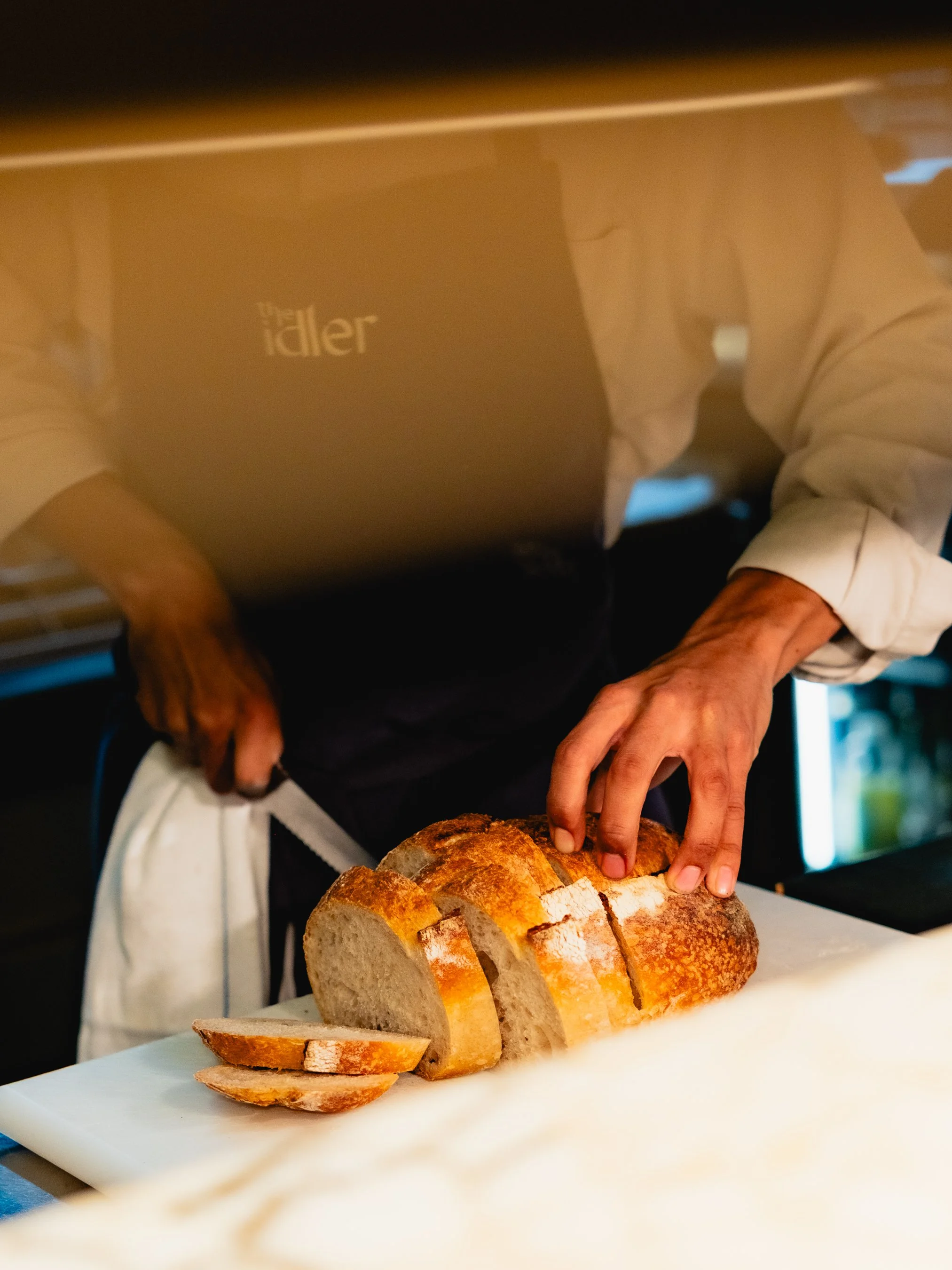 Person slicing a loaf of bread on a white cutting board in a kitchen.