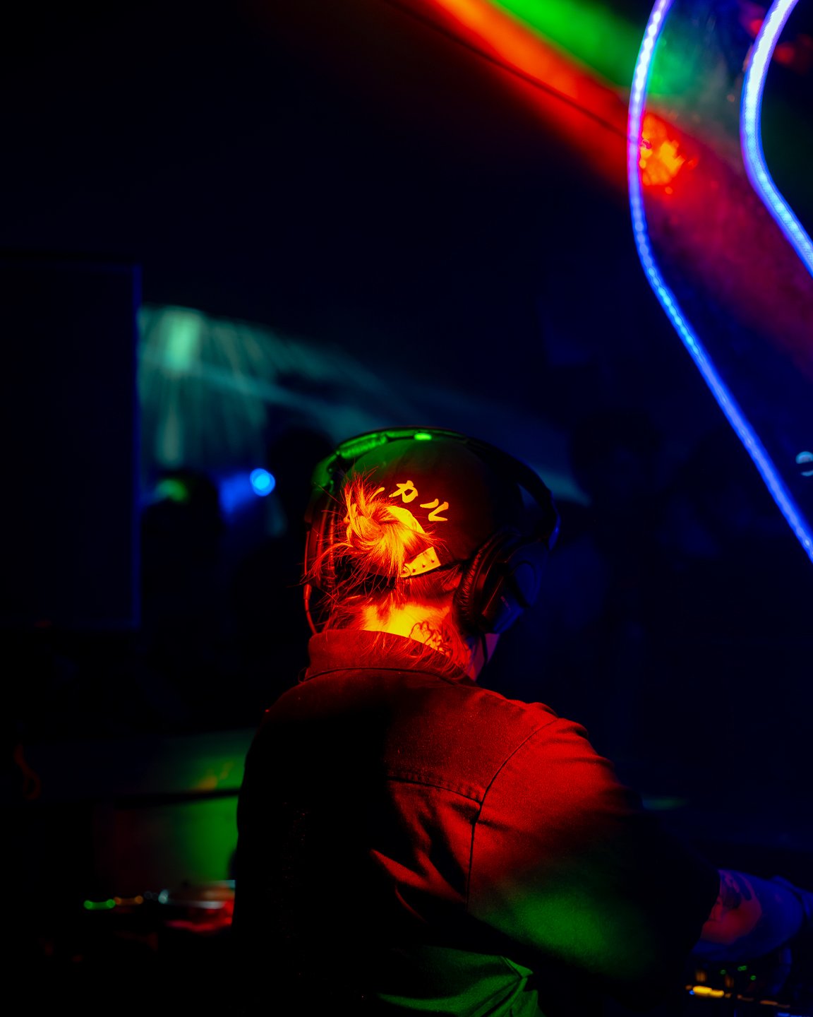 A person with a tattoo on the back of their neck is wearing headphones with the word 'Pony' illuminated in lights, in a dark room with colorful LED lights creating a vibrant atmosphere, likely at a party or concert.