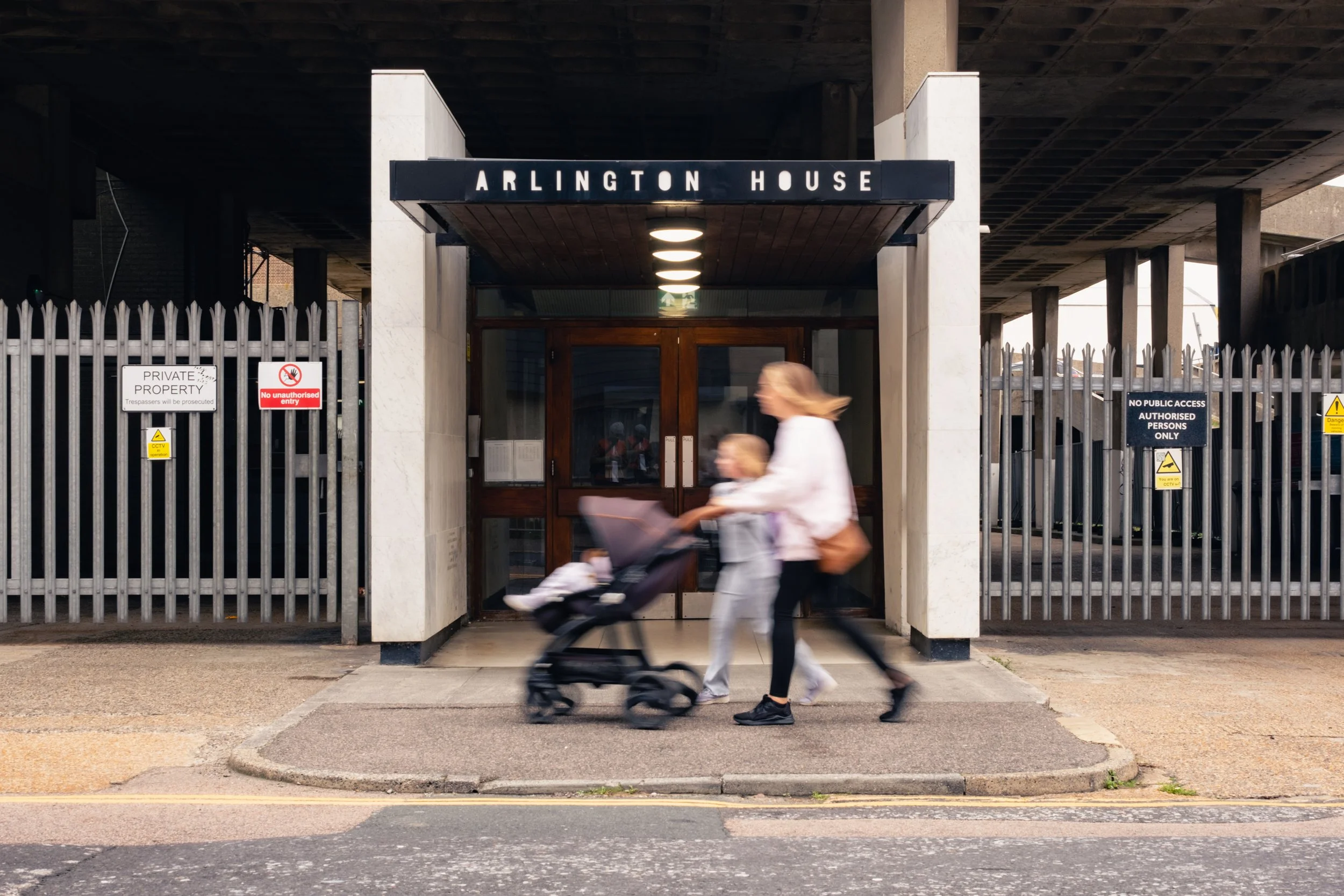 The entrance to Arlington House with a sign above the doorway. Two people are walking and pushing a stroller past the entrance.