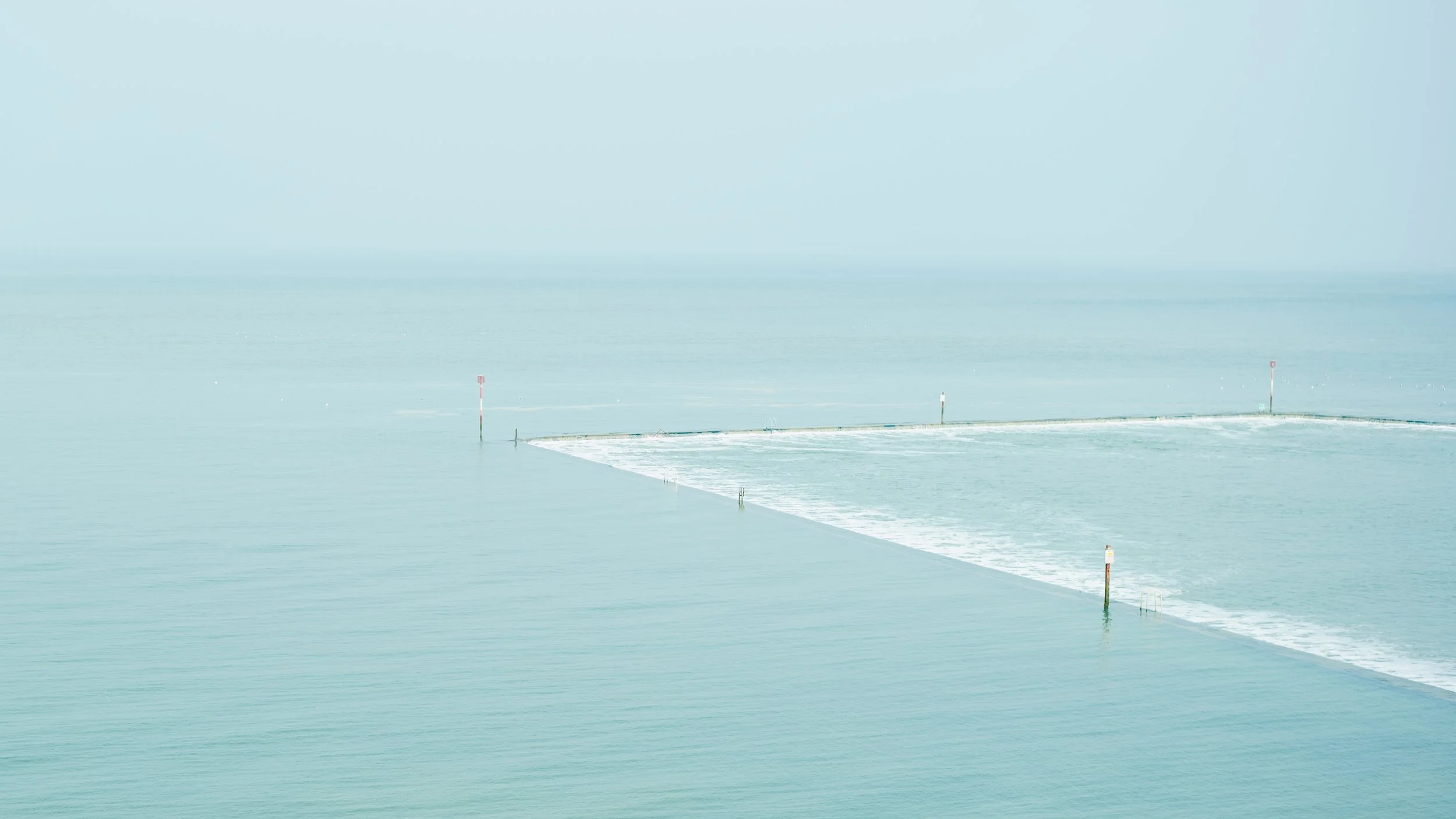 A pier extending into Calm ocean waters on a cloudy day, with four navigation markers in the water.