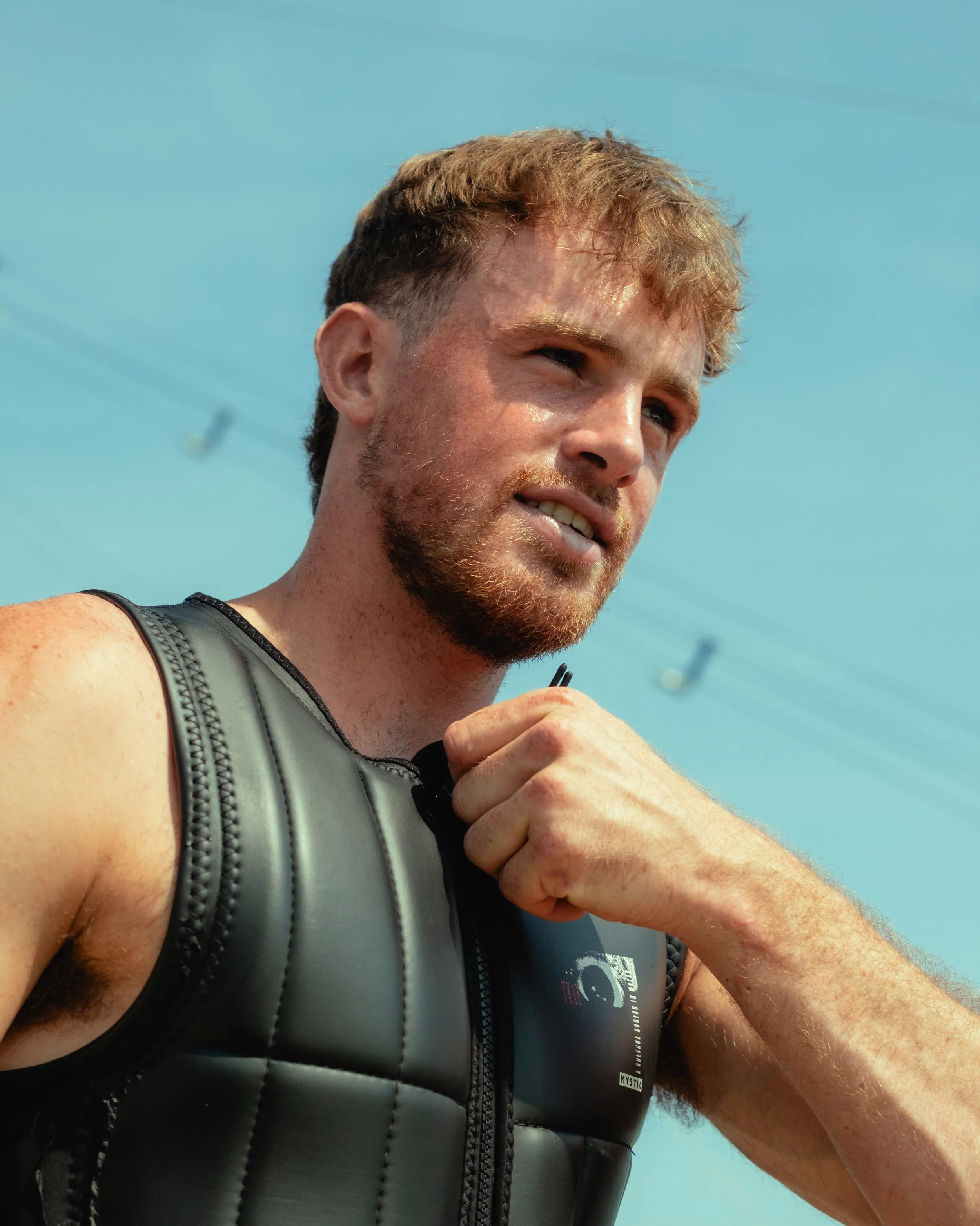Close-up of a man in a black athletic vest taking a selfie outdoors, with a clear blue sky in the background.