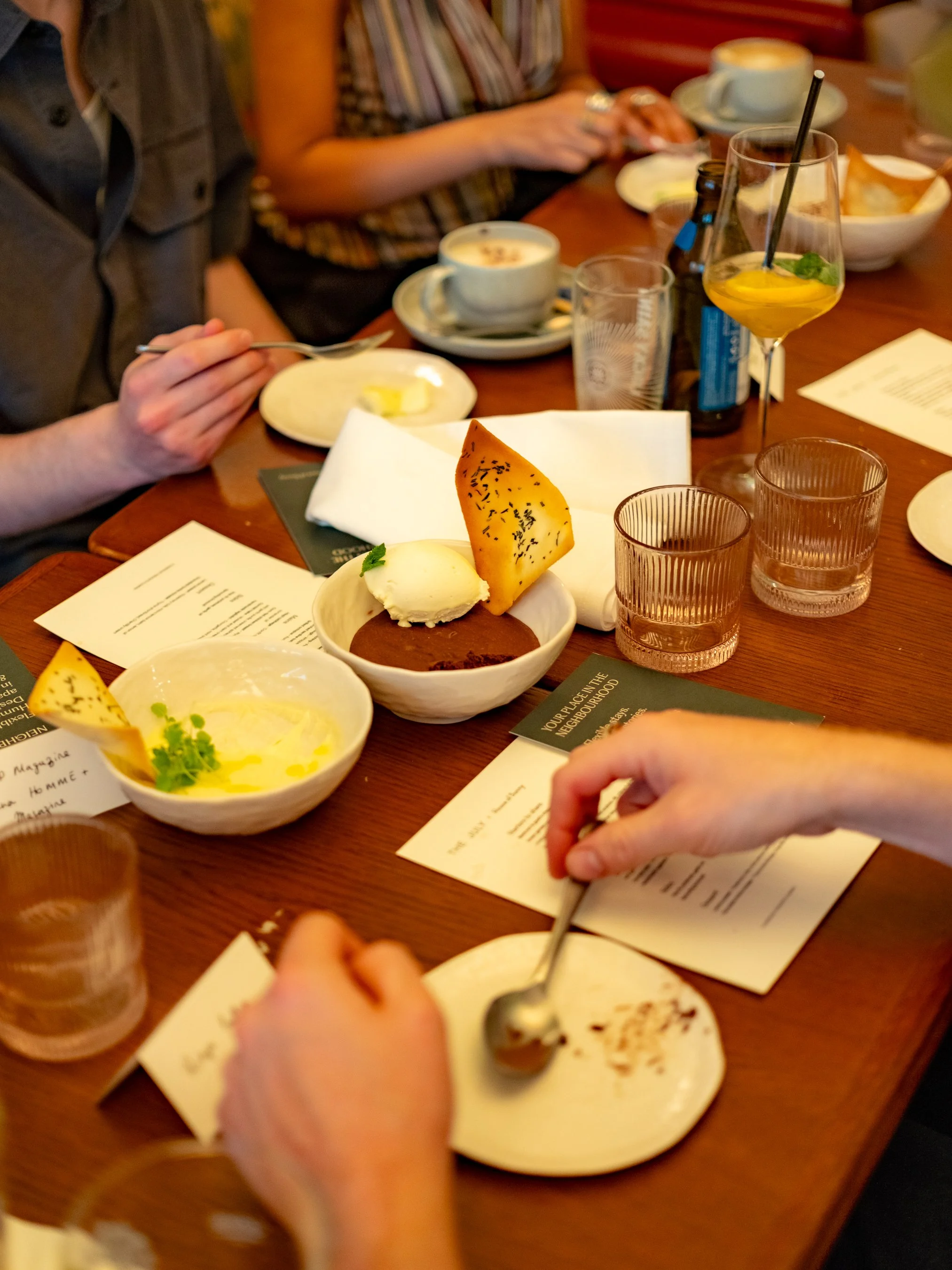 People sitting at a table enjoying desserts and drinks in a restaurant, with plates of chocolate and ice cream, and a cocktail with lemon and mint.