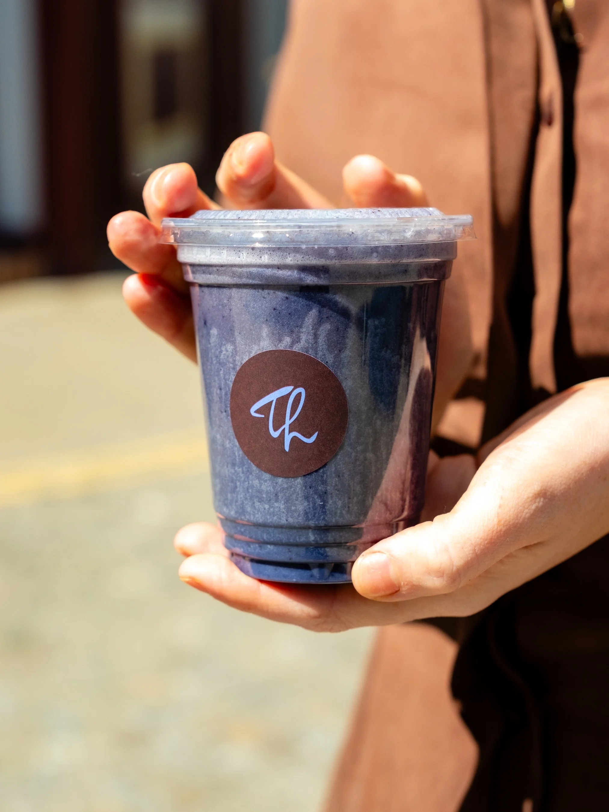 A person holding a blue paper cup with a clear plastic lid.