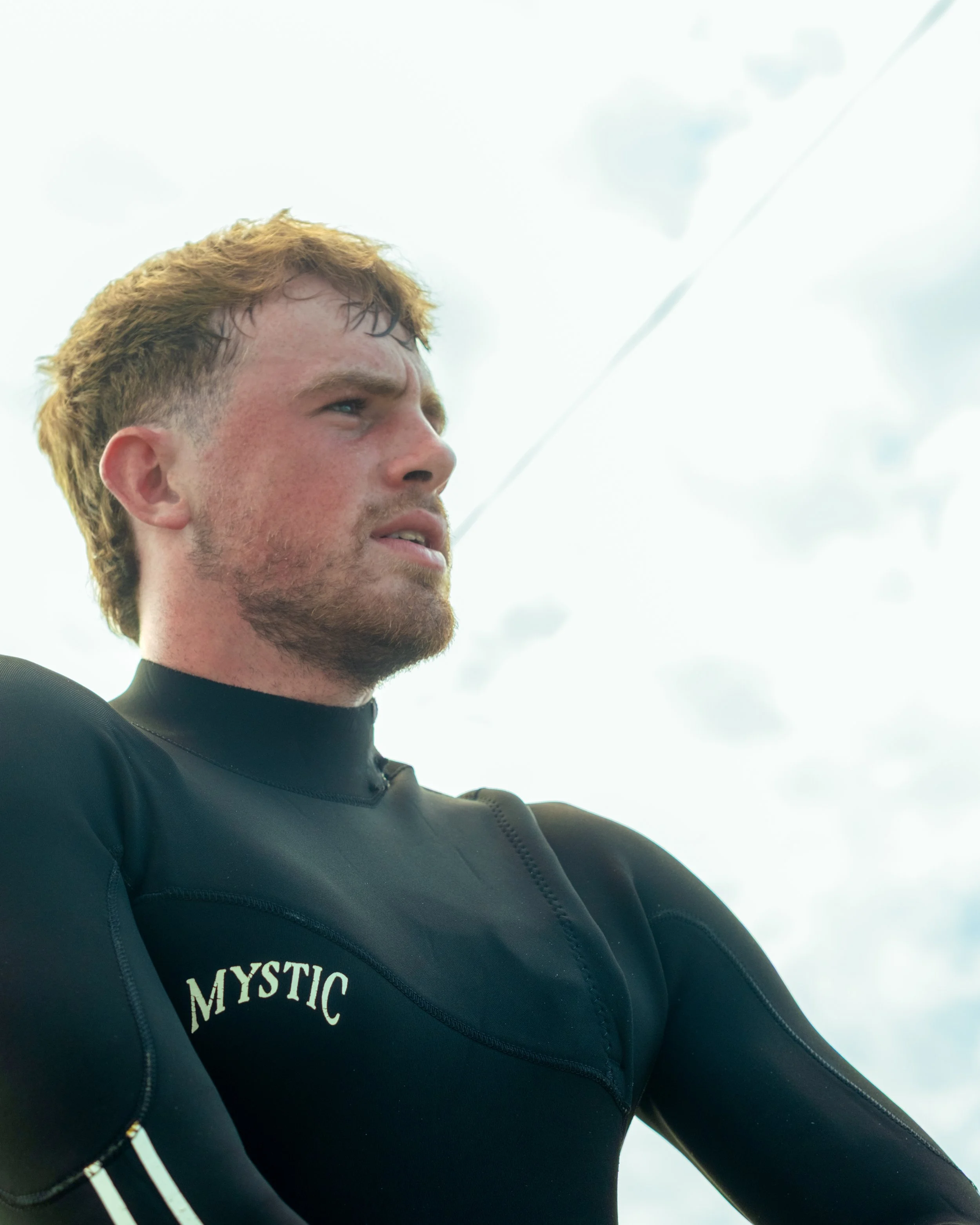 Close-up of a young man with reddish hair and a beard, wearing a black wetsuit.