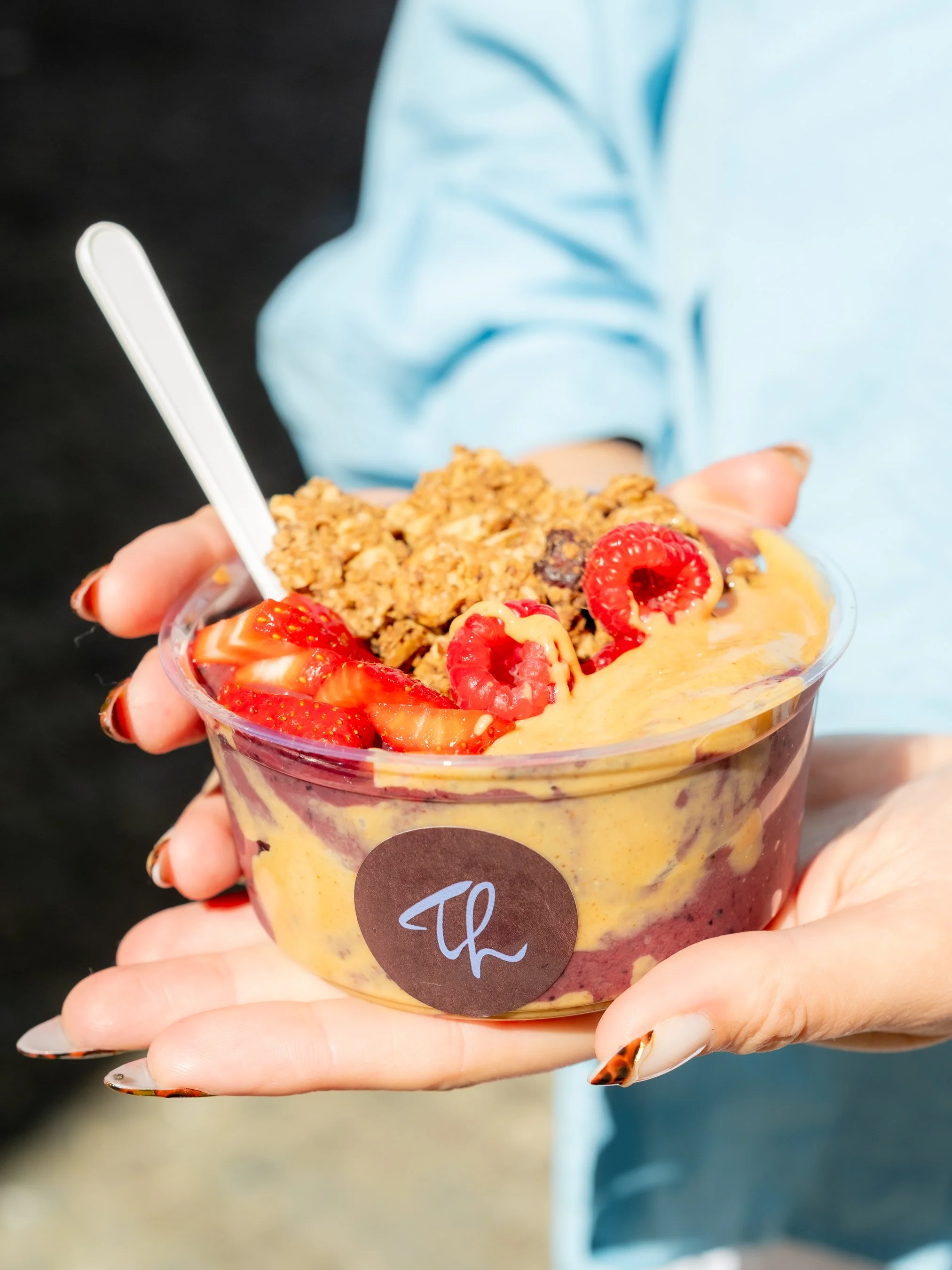 Person holding a cup of layered yogurt with strawberries, granola, and sauce