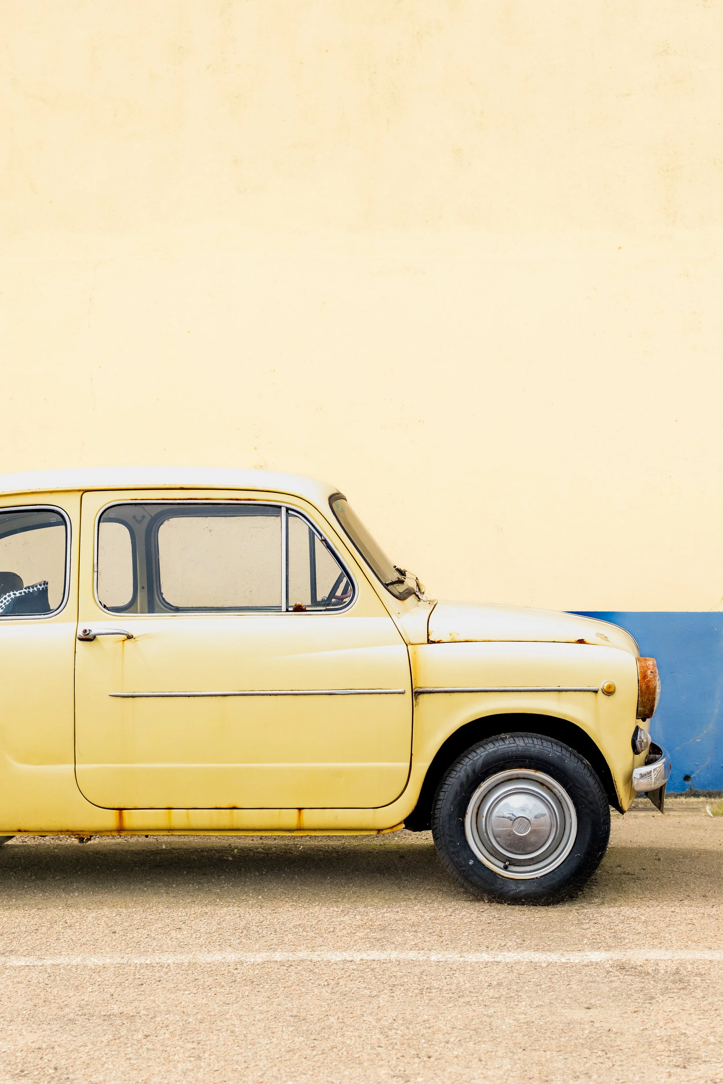 A vintage yellow taxi cab parked beside a building with a beige wall.