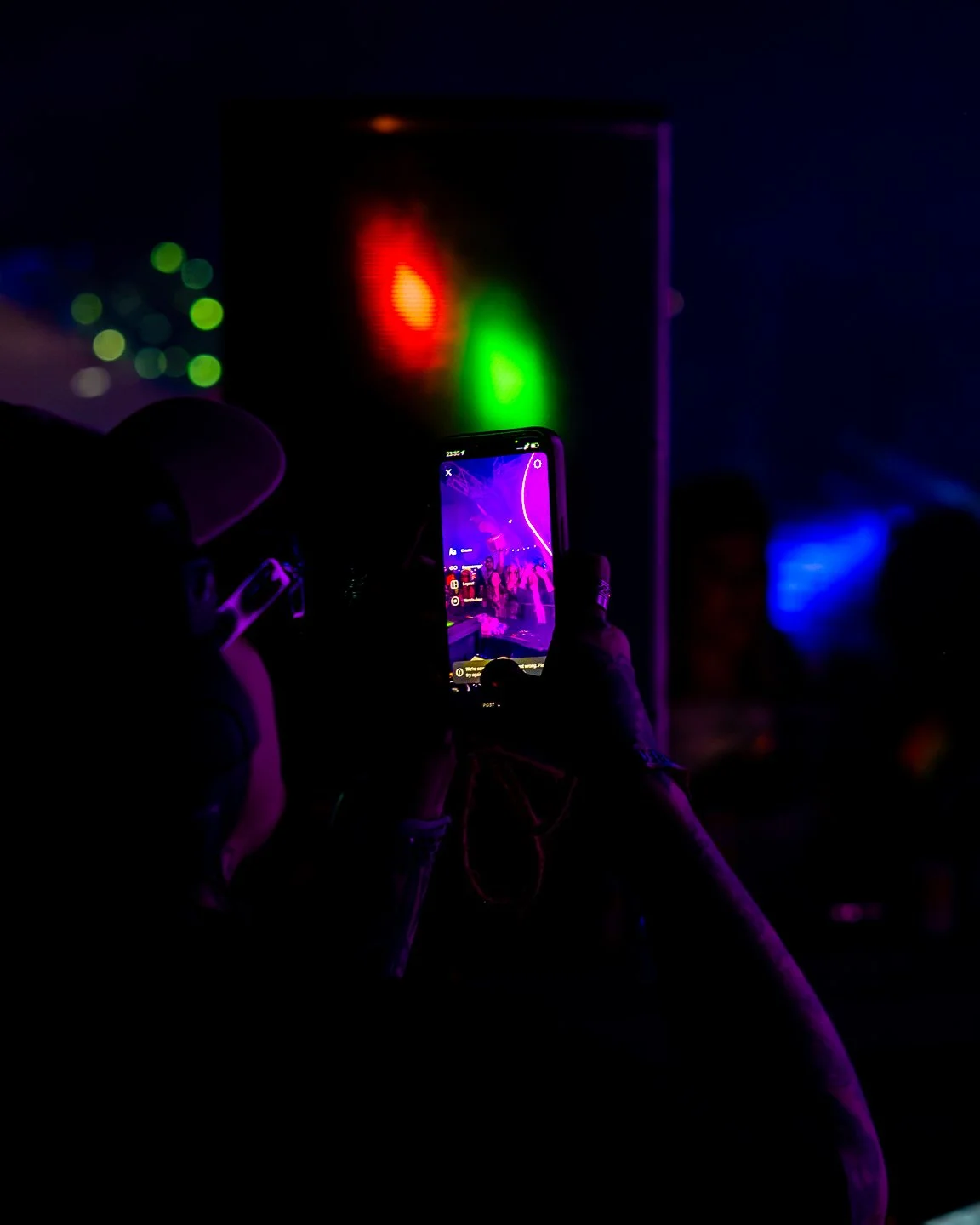 Person taking a photo of a colorful light display on a screen at a night event.