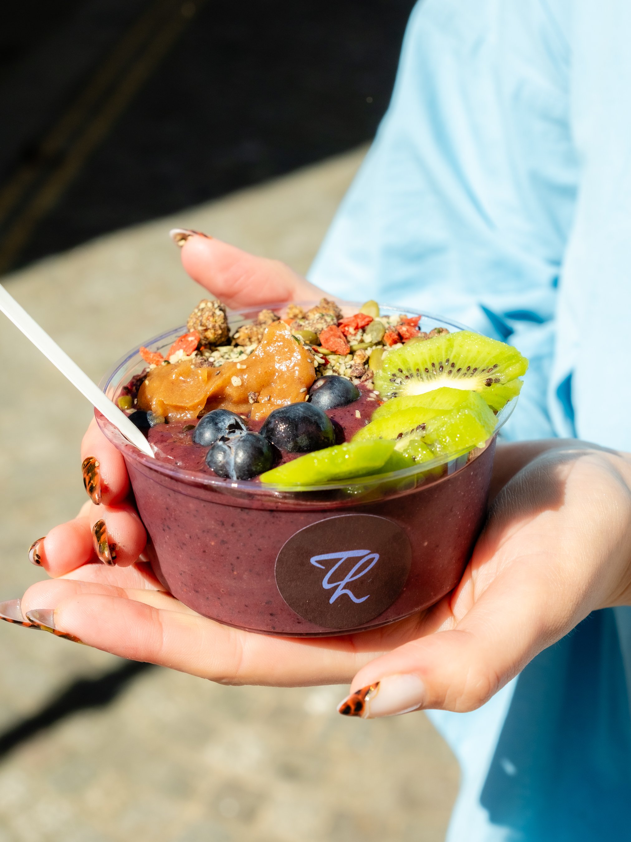 Person holding a clear cup filled with mixed berries, kiwi, granola, and peanut butter, with a white spoon inside.