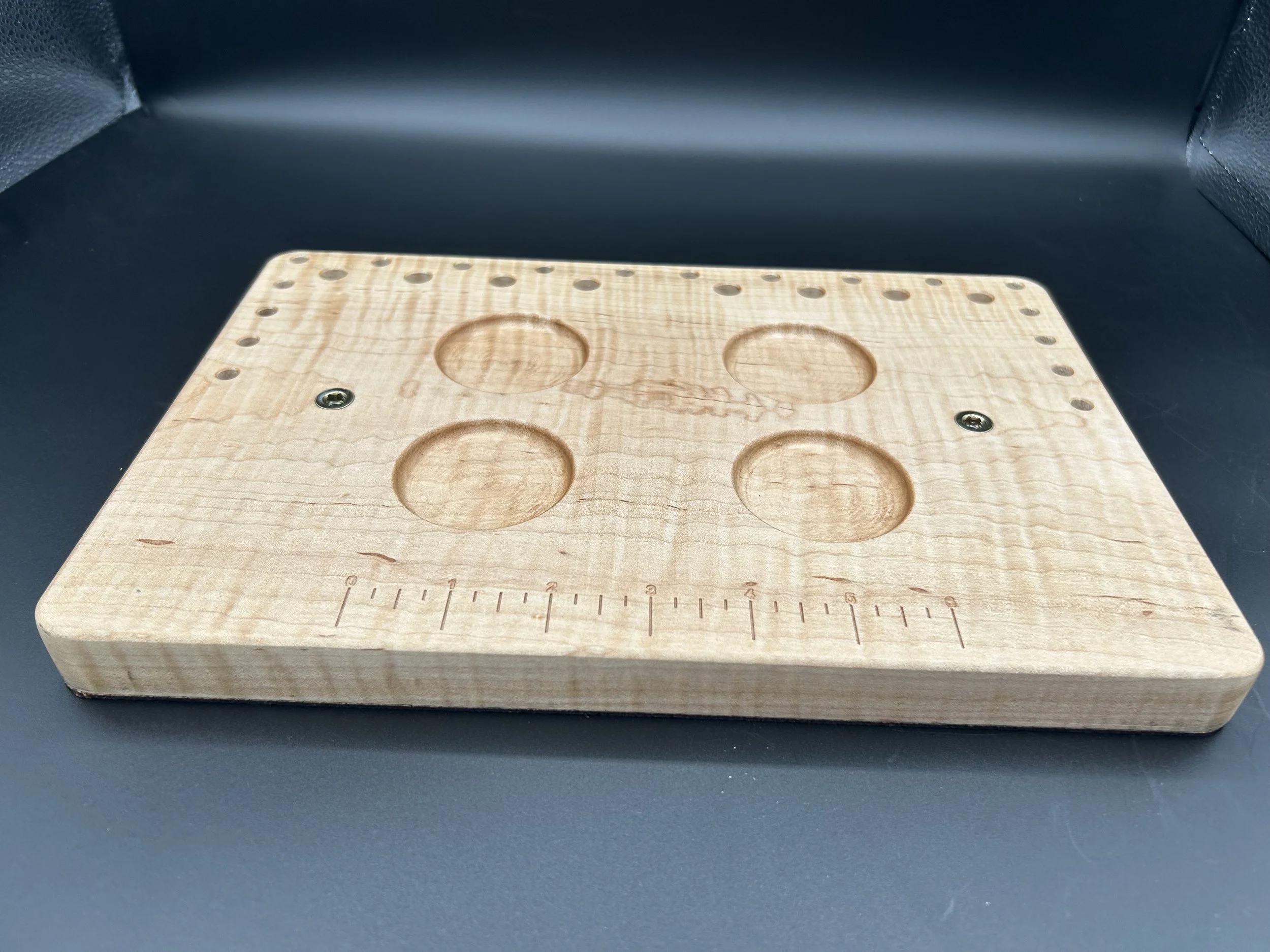 Wooden pegboard with circular indentations on a black surface.