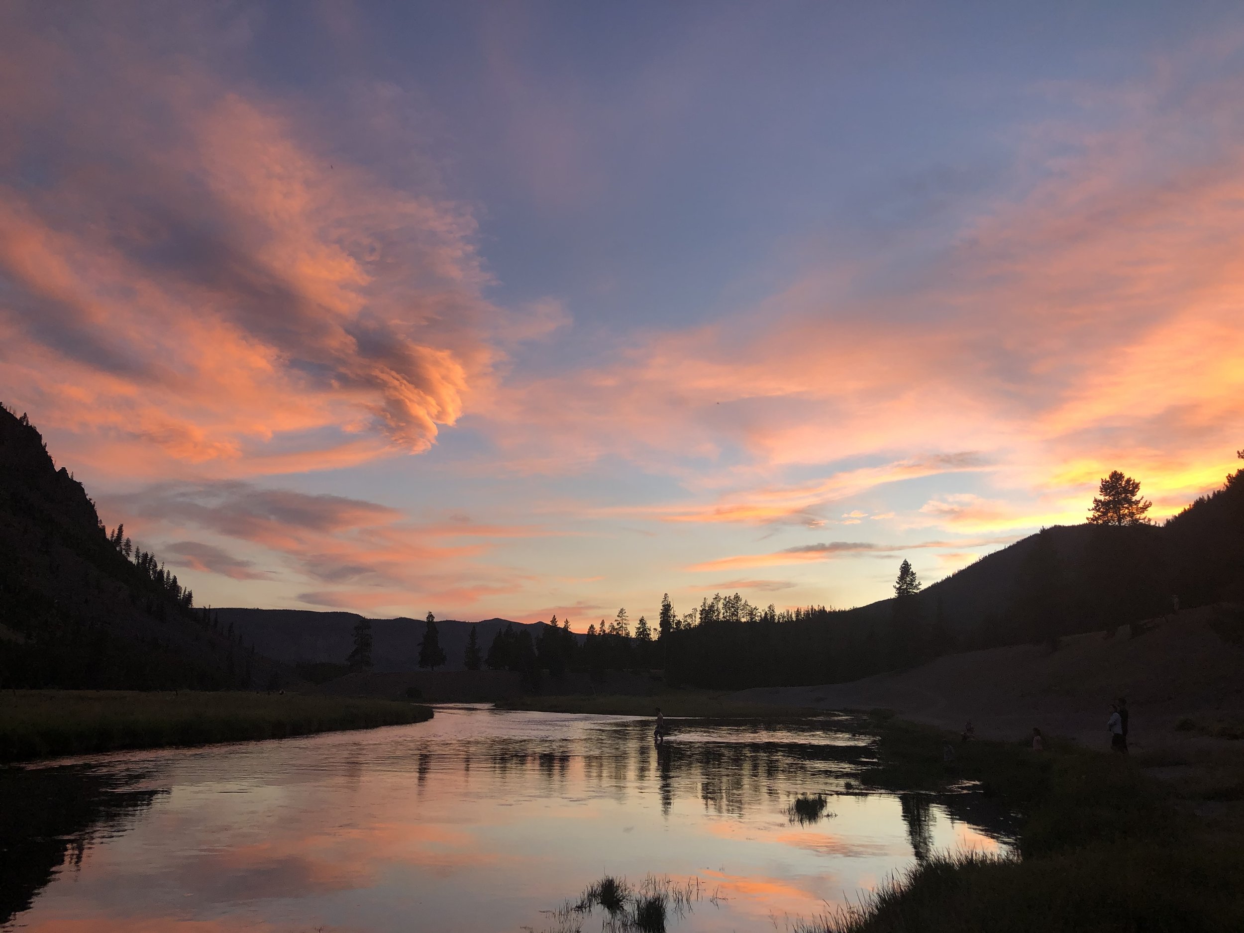 Scenic view of a river with mountains on either side during sunset, with colorful clouds in the sky.